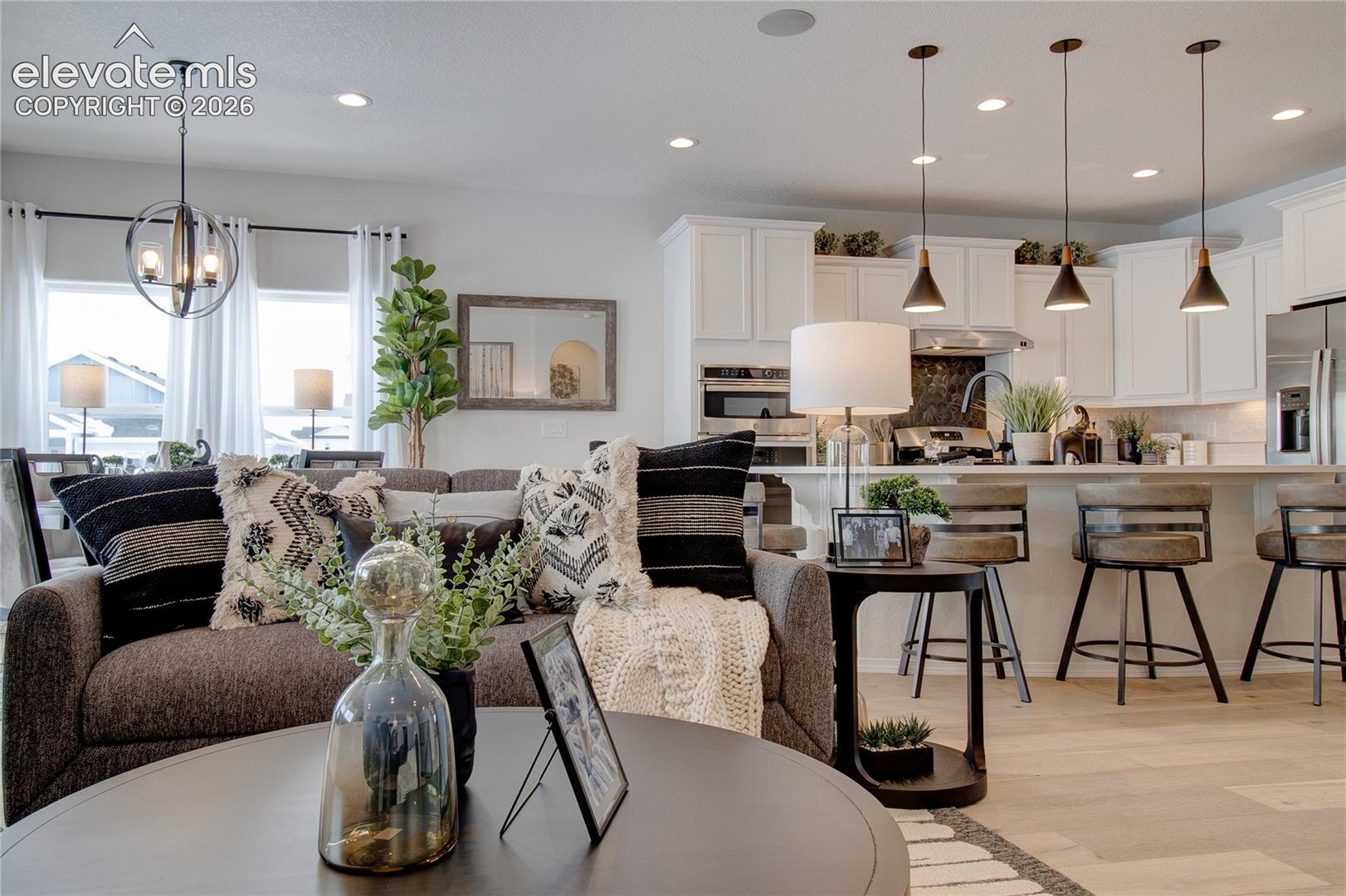 Open-concept living space featuring wood-finish flooring, white cabinetry, a center island with bar seating, pendant lighting, and a globe chandelier