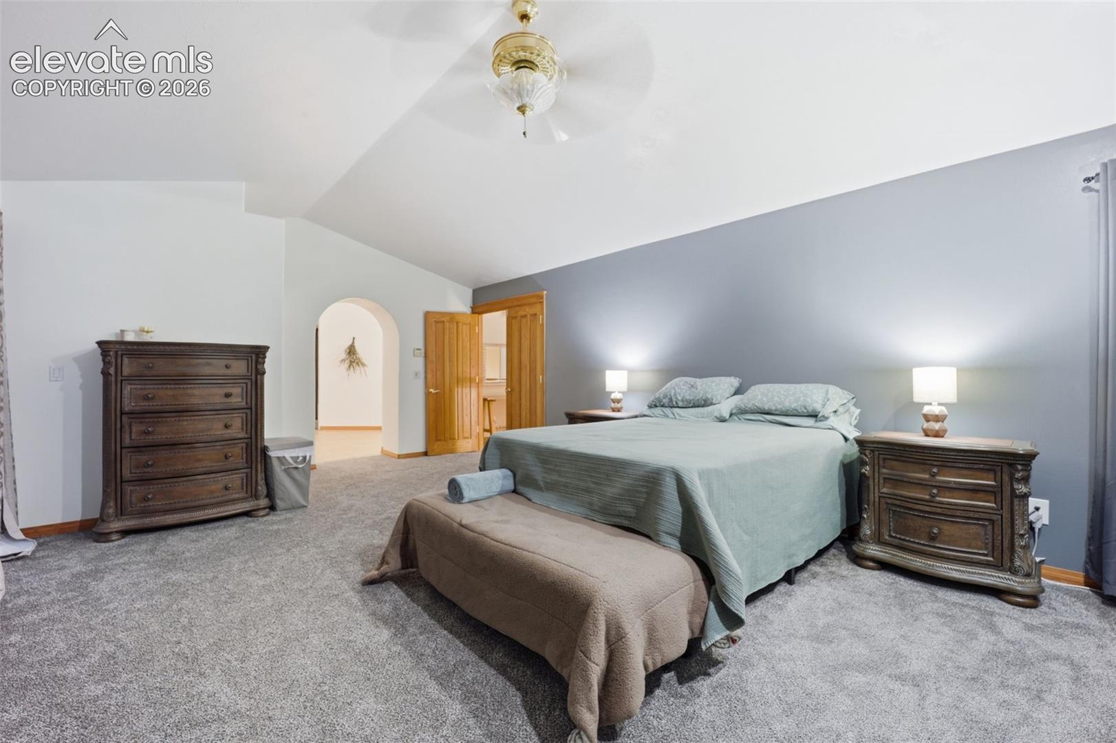 Vaulted ceiling with a ceiling fan, arched doorway, and wood-finish doors