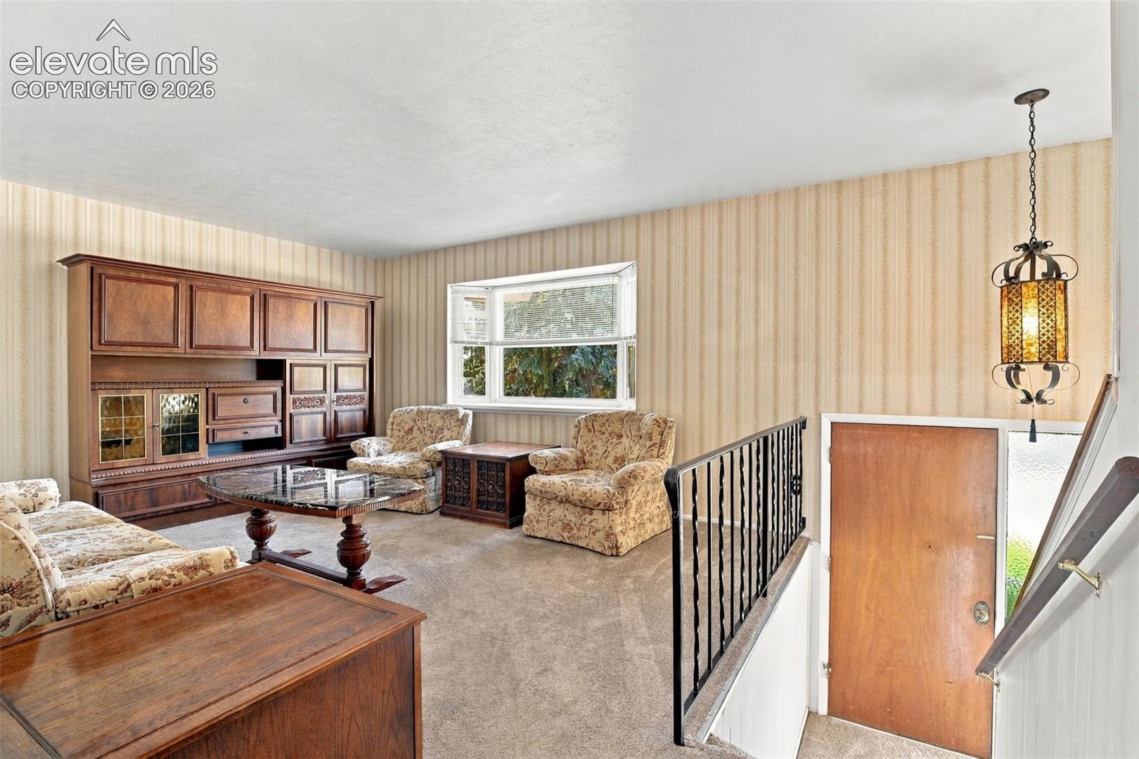 Interior space featuring built-in wooden cabinetry, a large bay window, a metal staircase railing, and a decorative hanging light fixture