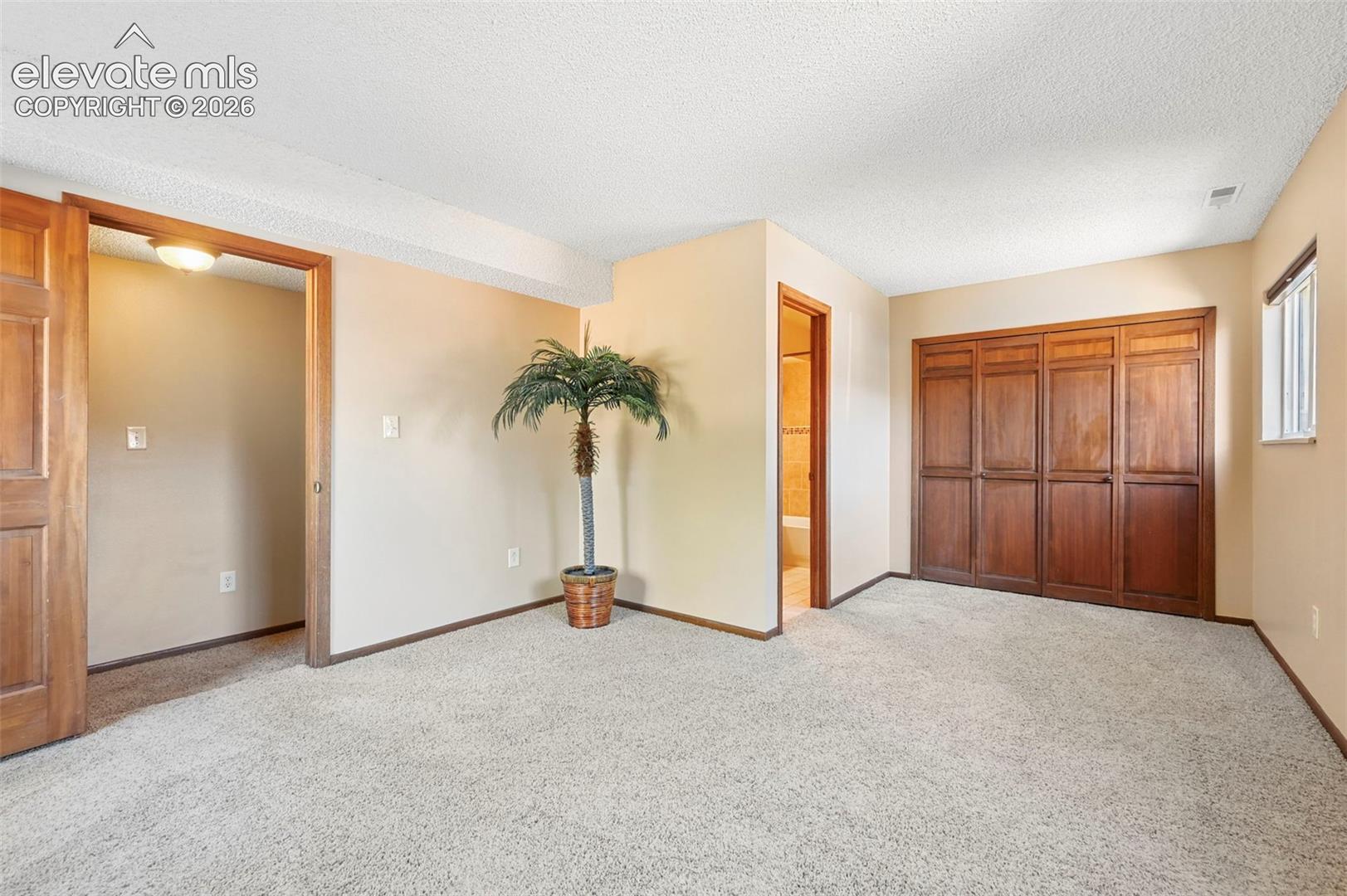 Room interior featuring neutral wall paint, wall-to-wall carpeting, wood-finish closet doors, and wood-finish door frames