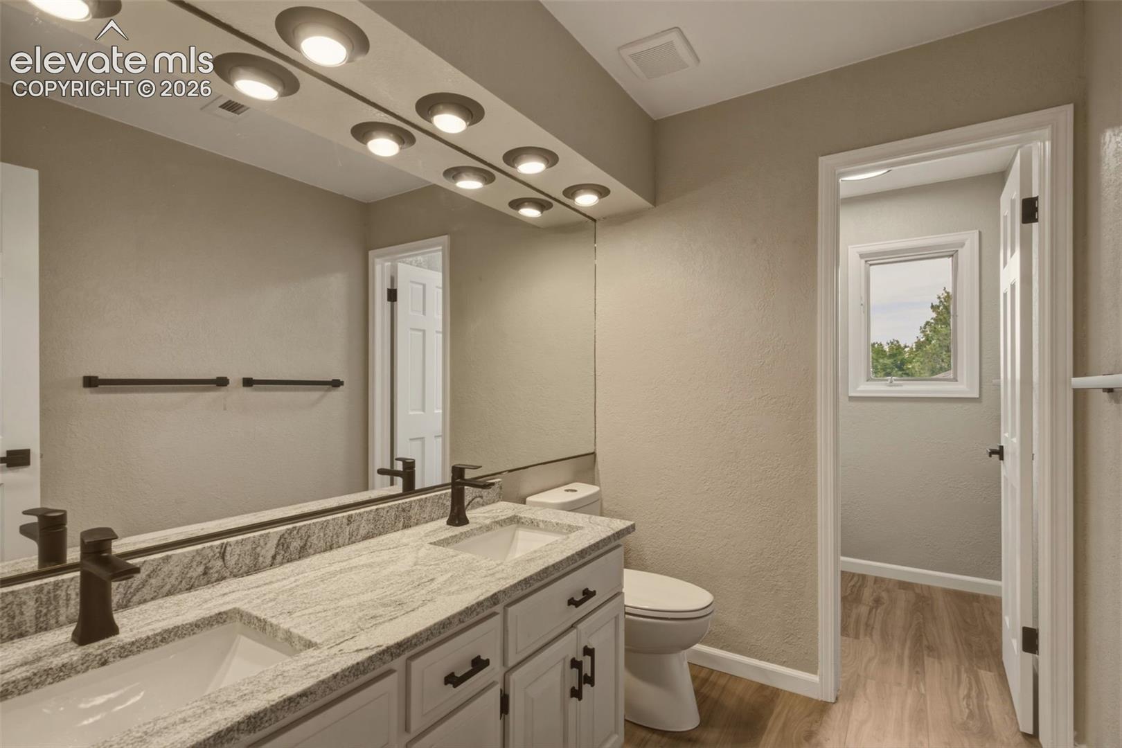 Double vanity with integrated sinks, granite-look countertop, white cabinetry, and wall-mounted lighting