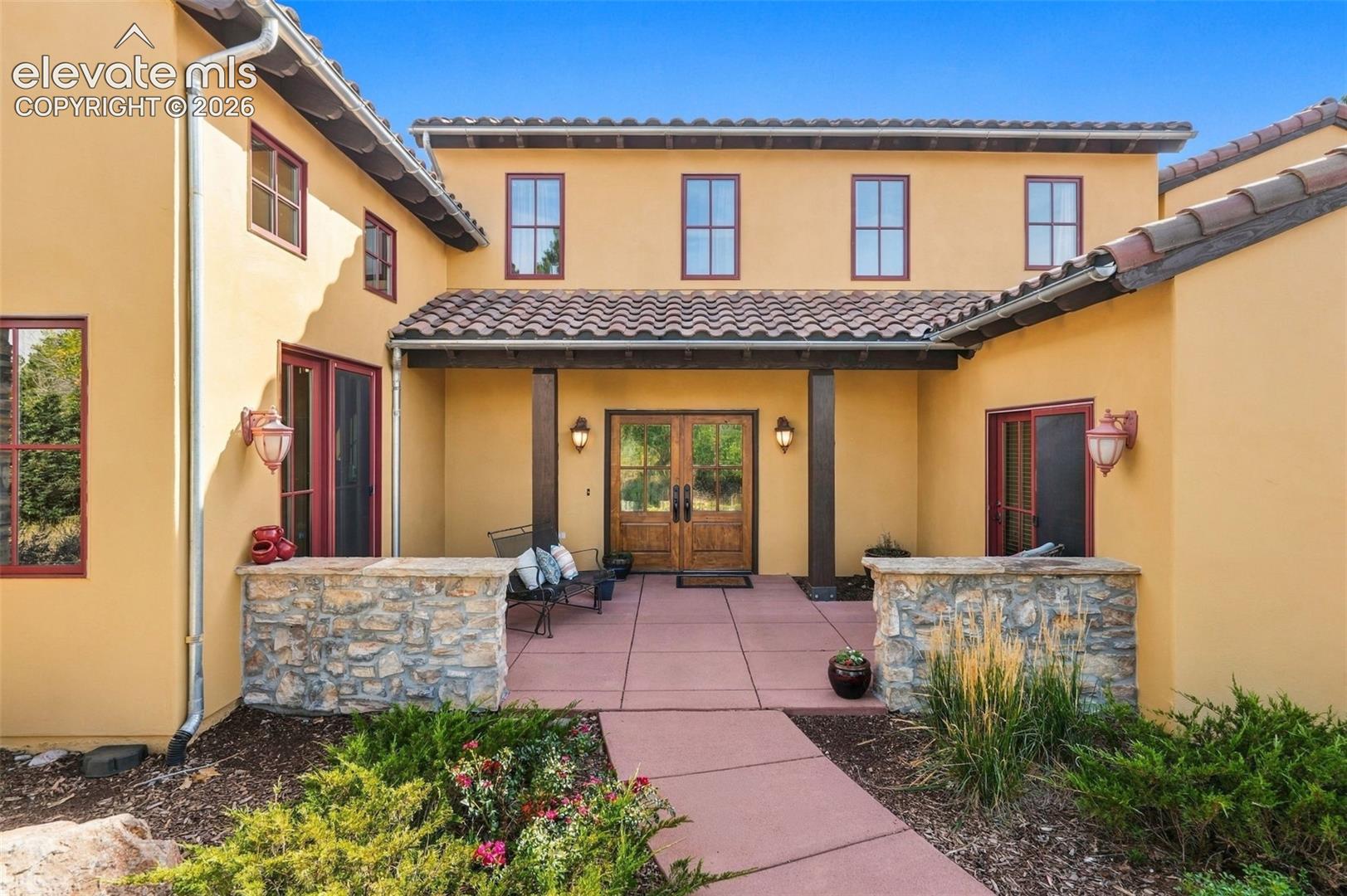 Stucco exterior with a tile roof, covered entry, double wood entry doors, and stone accents