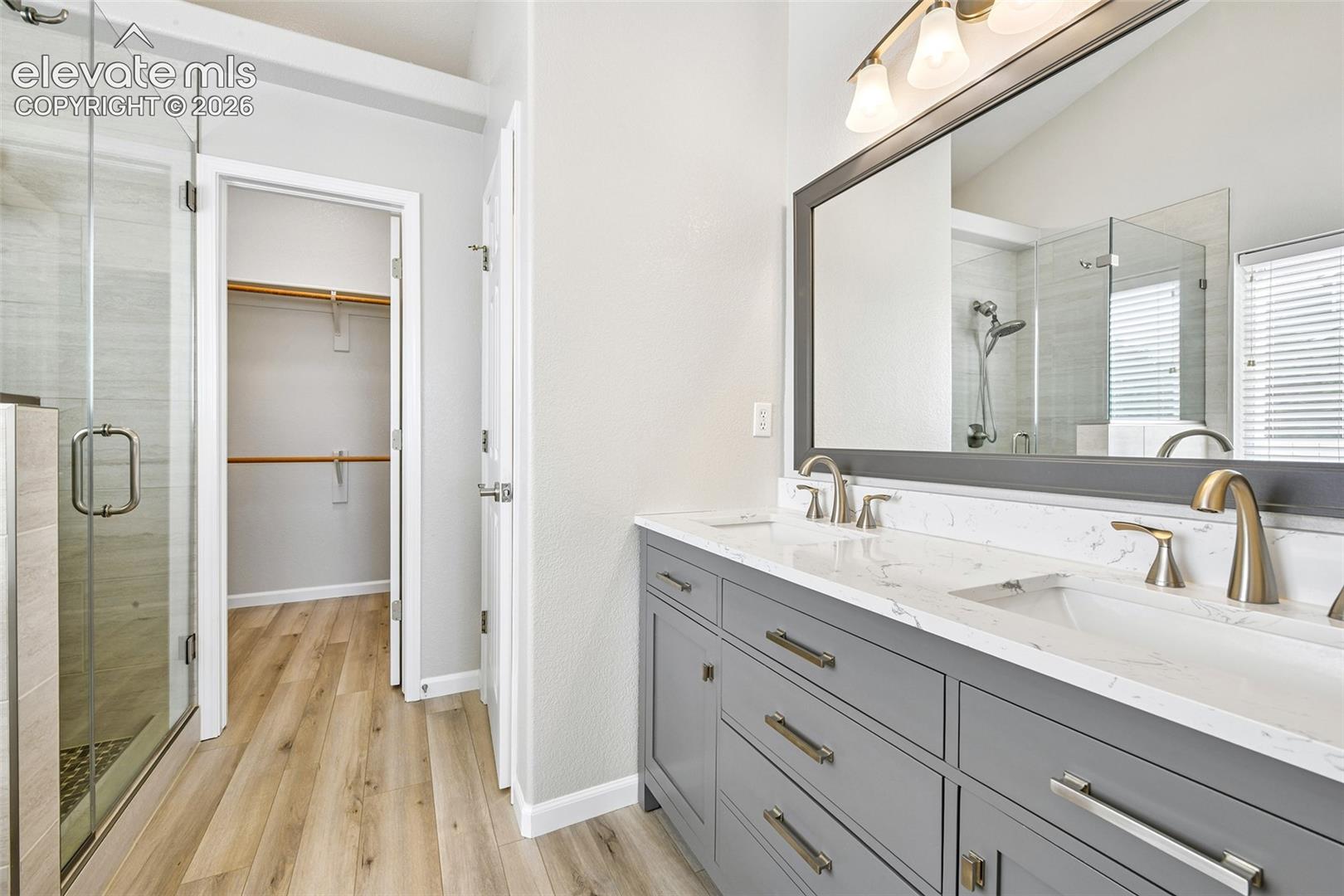 Dual vanity with quartz-finish countertop and undermount sinks, wood-finish flooring, glass-enclosed shower, and sloped ceiling
