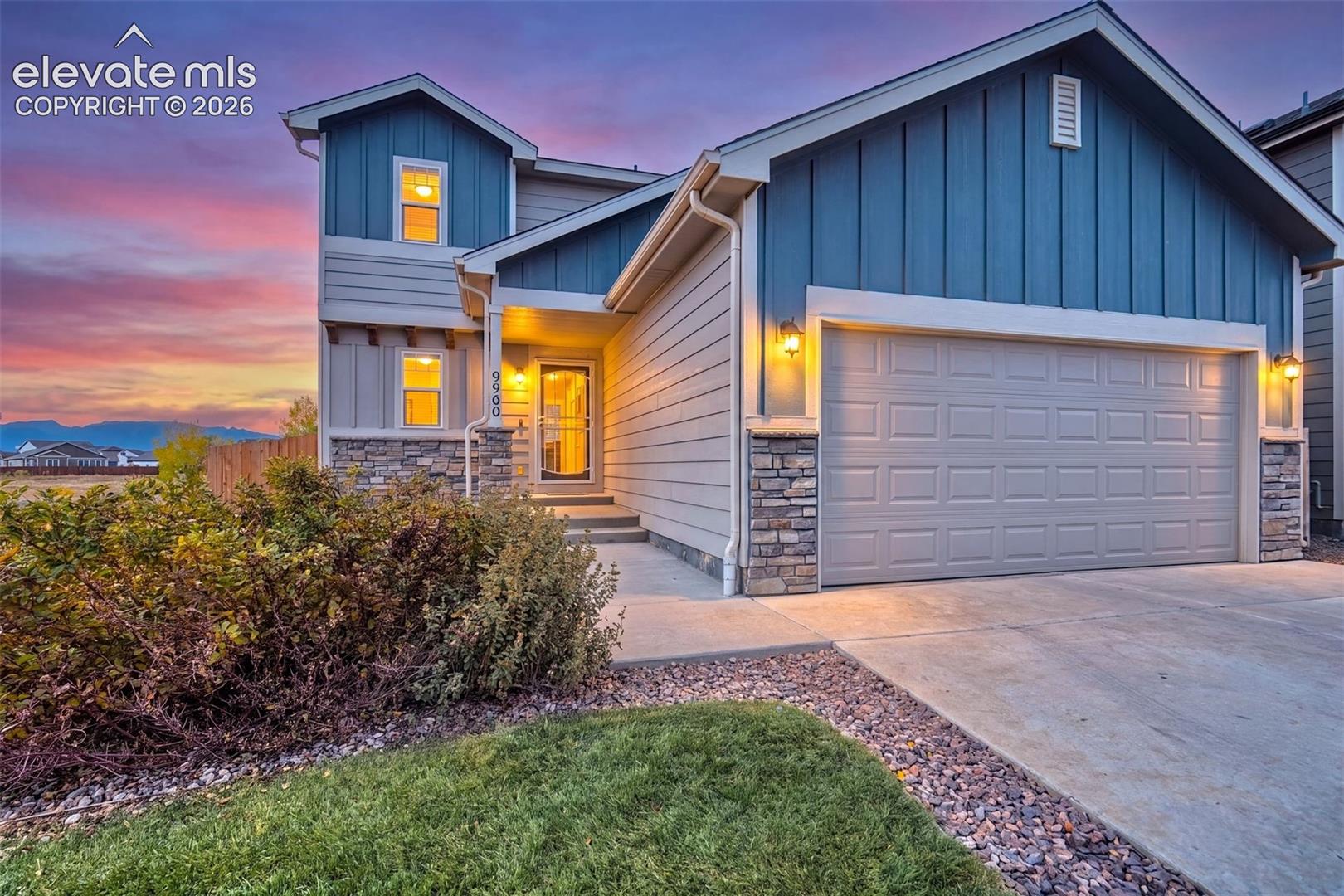 Two-story residence featuring vertical and horizontal siding, stone veneer accents, a multi-car garage, and concrete driveway