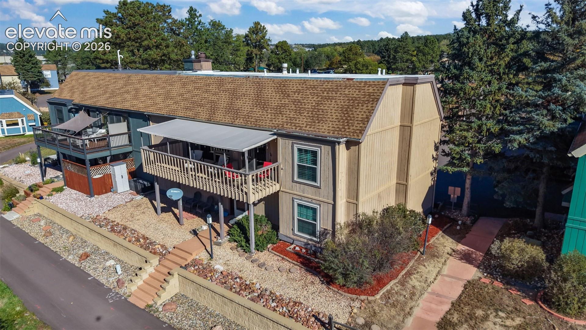 Multi-level exterior featuring a shingled roof, elevated wood deck with an attached canopy, vertical siding, and concrete retaining walls