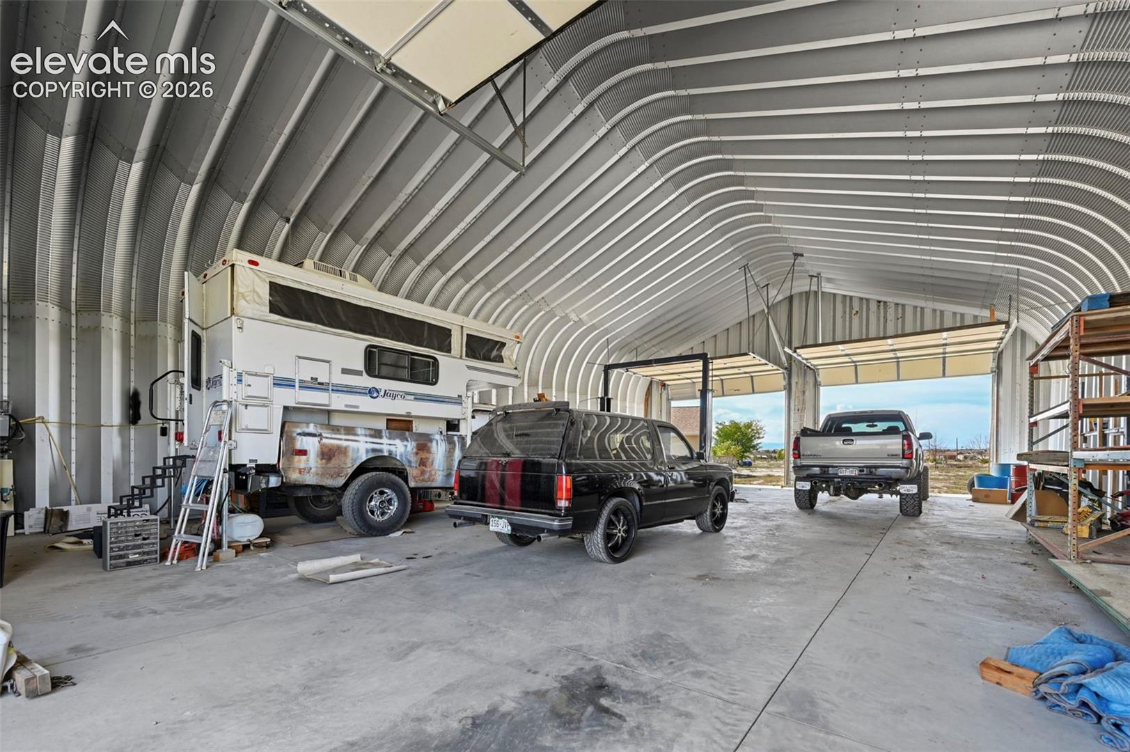 Spacious metal Quonset-style structure featuring a high-clearance arched ceiling, concrete flooring, and multiple overhead industrial garage doors