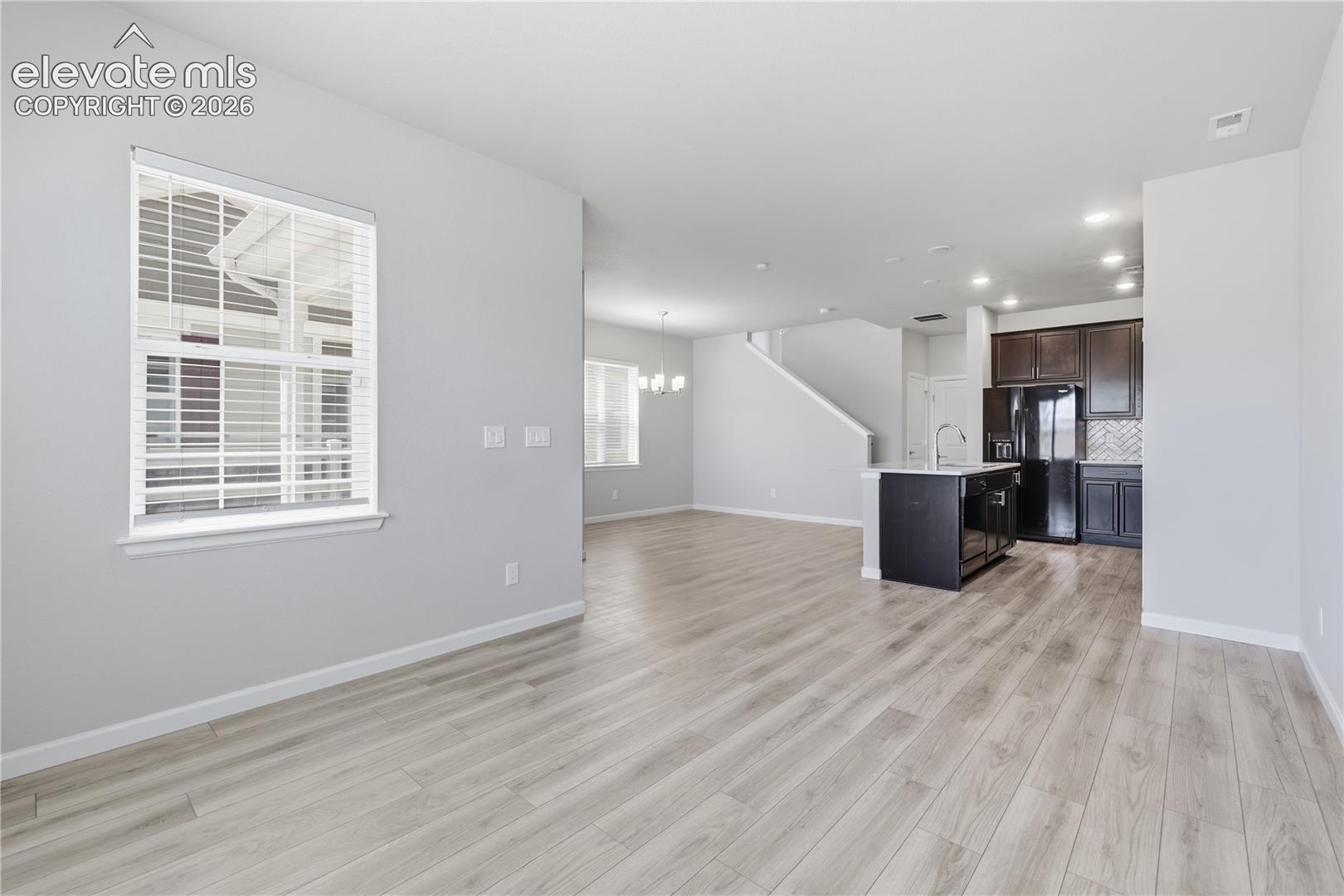 Open-concept living space with light wood-finish flooring, recessed lighting, a modern kitchen island, dark wood cabinetry, and a full-size refrigerator