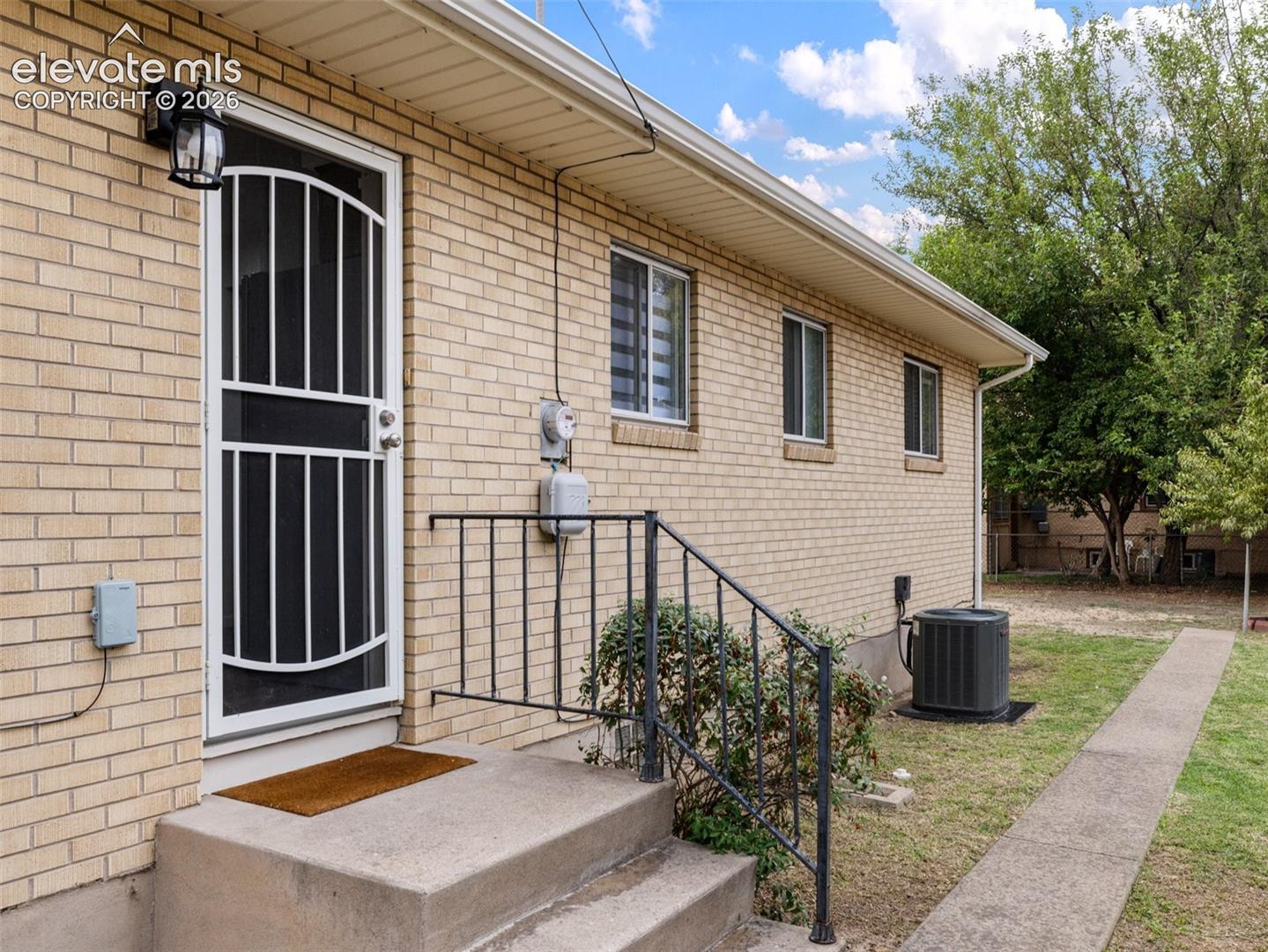 Brick exterior with a security screen door, exterior lighting, concrete steps, and a wrought iron handrail