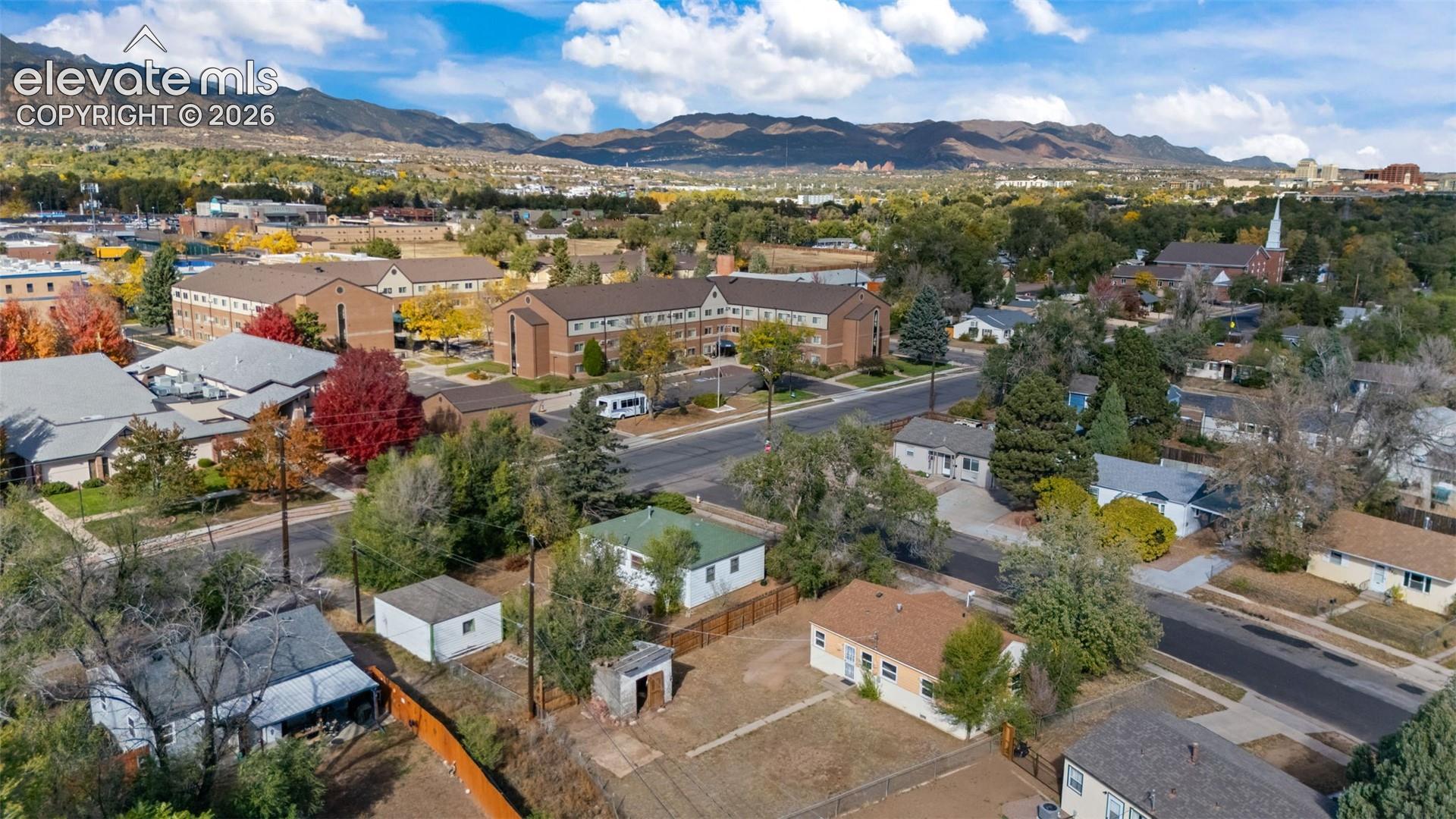 Aerial perspective of a residential parcel with mature trees, hardscaping, and mountain range backdrop