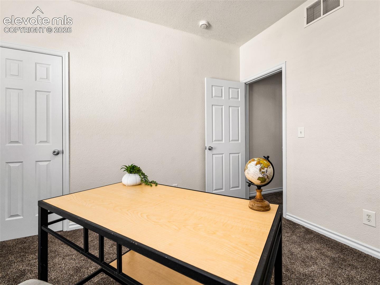 Textured walls in a neutral tone, white trim, and brown carpet flooring