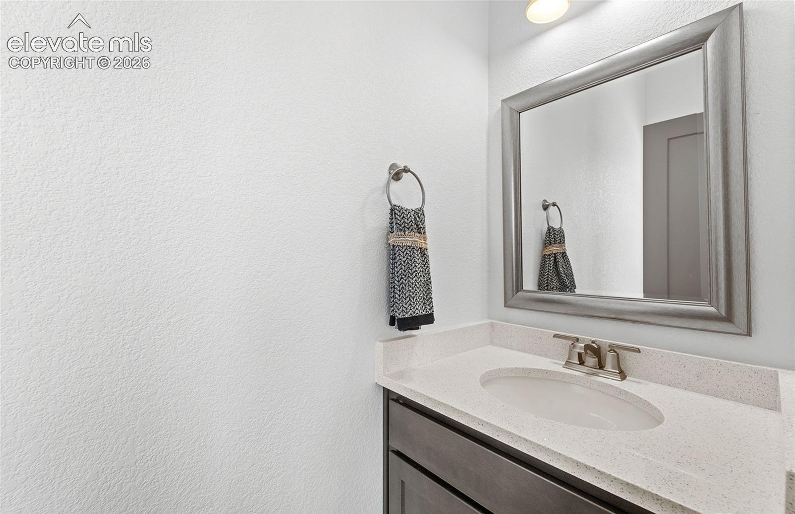 Stone-composite countertop featuring an integrated oval basin, dark-finish cabinetry, brushed-nickel faucet, and a wall-mounted framed mirror