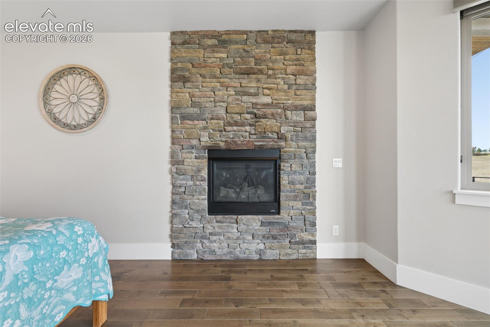 Floor-to-ceiling stone-clad fireplace with a black firebox, wood-finish flooring, and a window with white trim