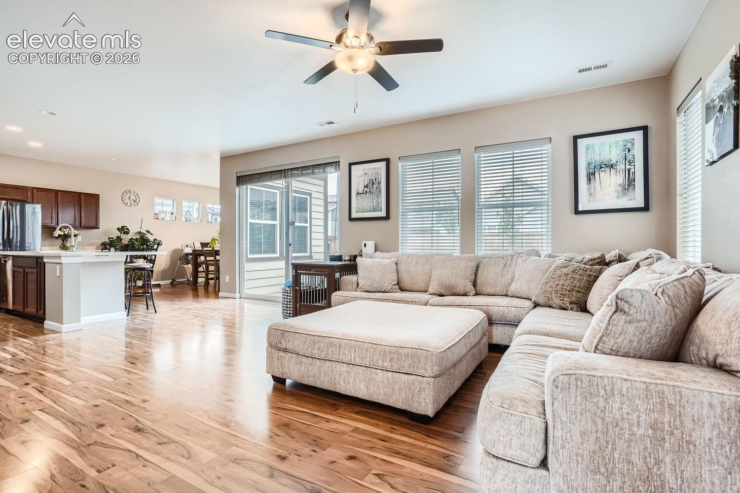 Open-concept living space featuring wood-finish flooring, recessed lighting, a ceiling fan with integrated light fixture, horizontal blinds, and a sliding glass door