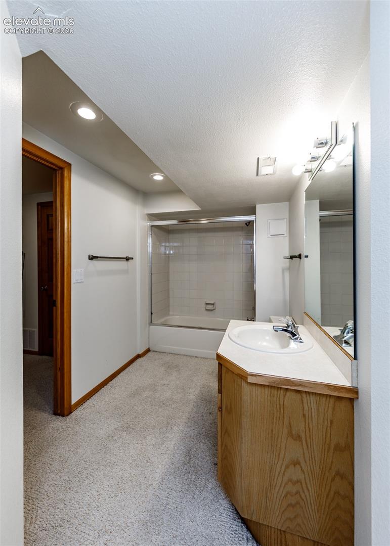 Bathroom featuring a white bathtub with tile surround, wood-finish vanity, integrated sink, and wall-mounted mirror