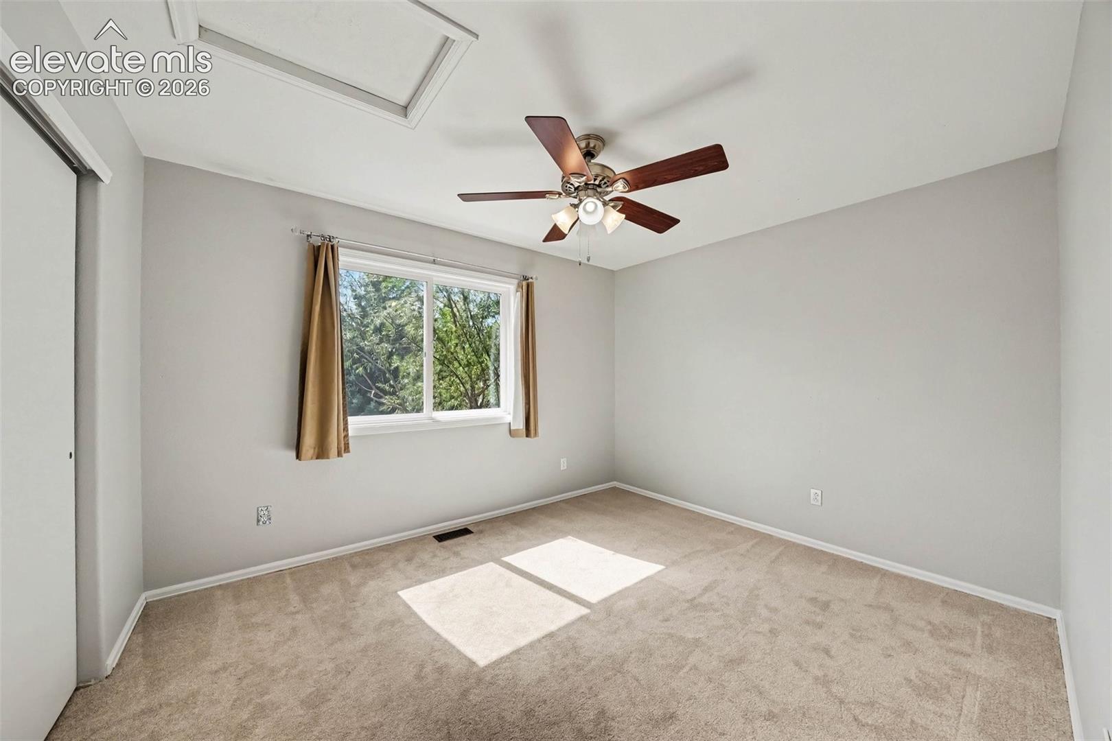Carpeted room featuring a ceiling fan with light fixture, a window, a skylight, and sliding closet doors