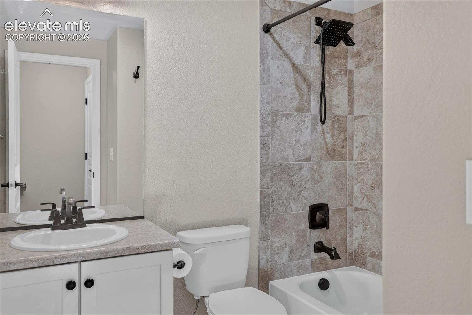 Bathroom featuring a shower-tub combination, tiled shower surround, dark bronze shower fixtures, and a vanity with a countertop sink