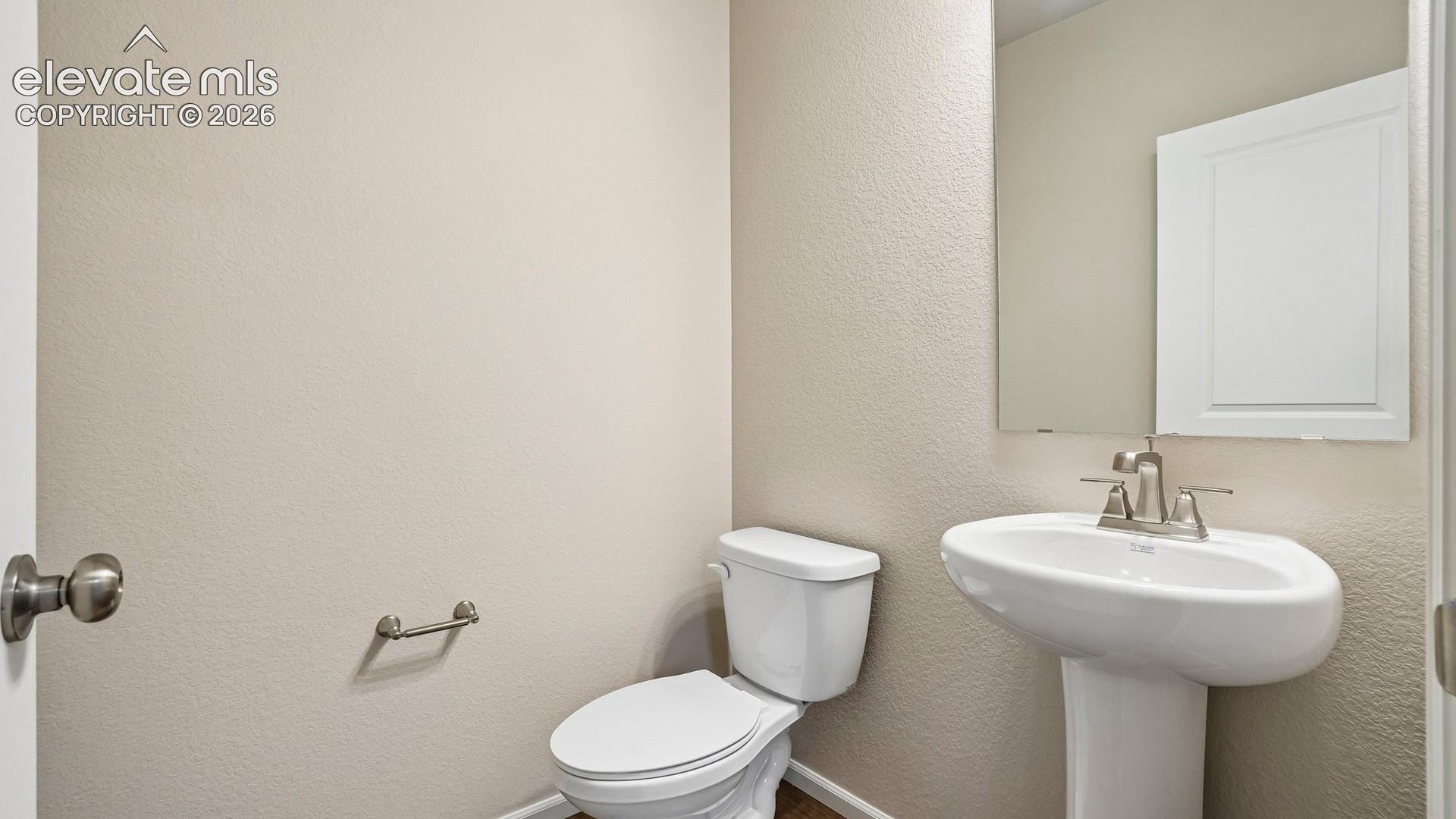 Pedestal sink with a polished chrome faucet, rectangular wall mirror, and a white toilet
*photos of a model home*
