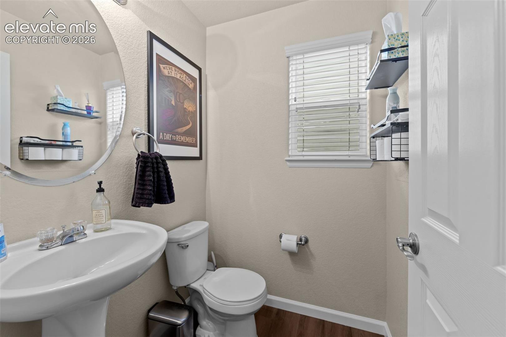 Pedestal sink with chrome faucet, circular wall mirror, and wood-finish flooring