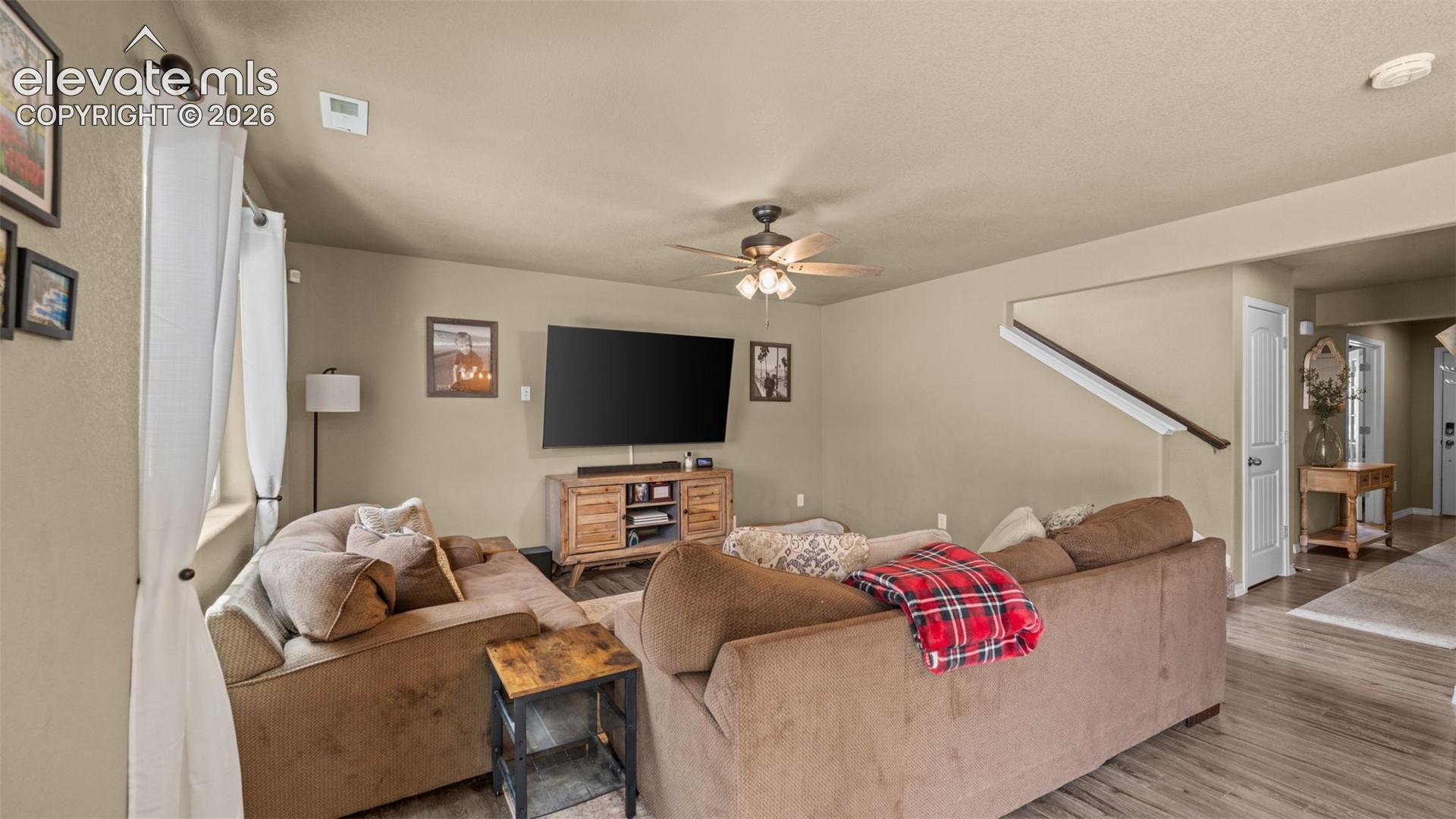 Spacious living area featuring wood-finish flooring, neutral wall tones, and a ceiling fan with integrated lighting