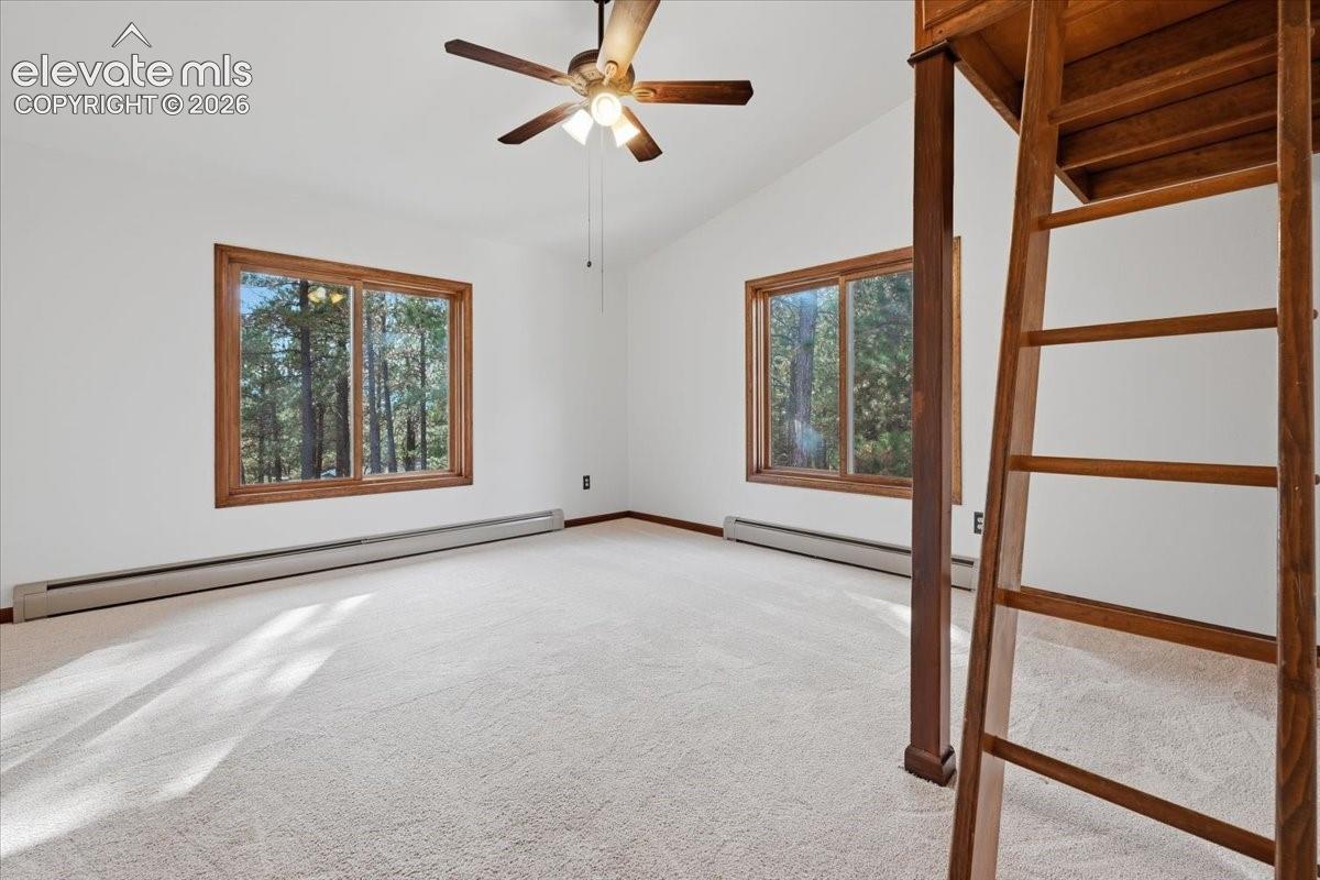 Vaulted ceiling with a ceiling fan, white wall paint, two large windows with natural wood frames, and light-colored carpeting