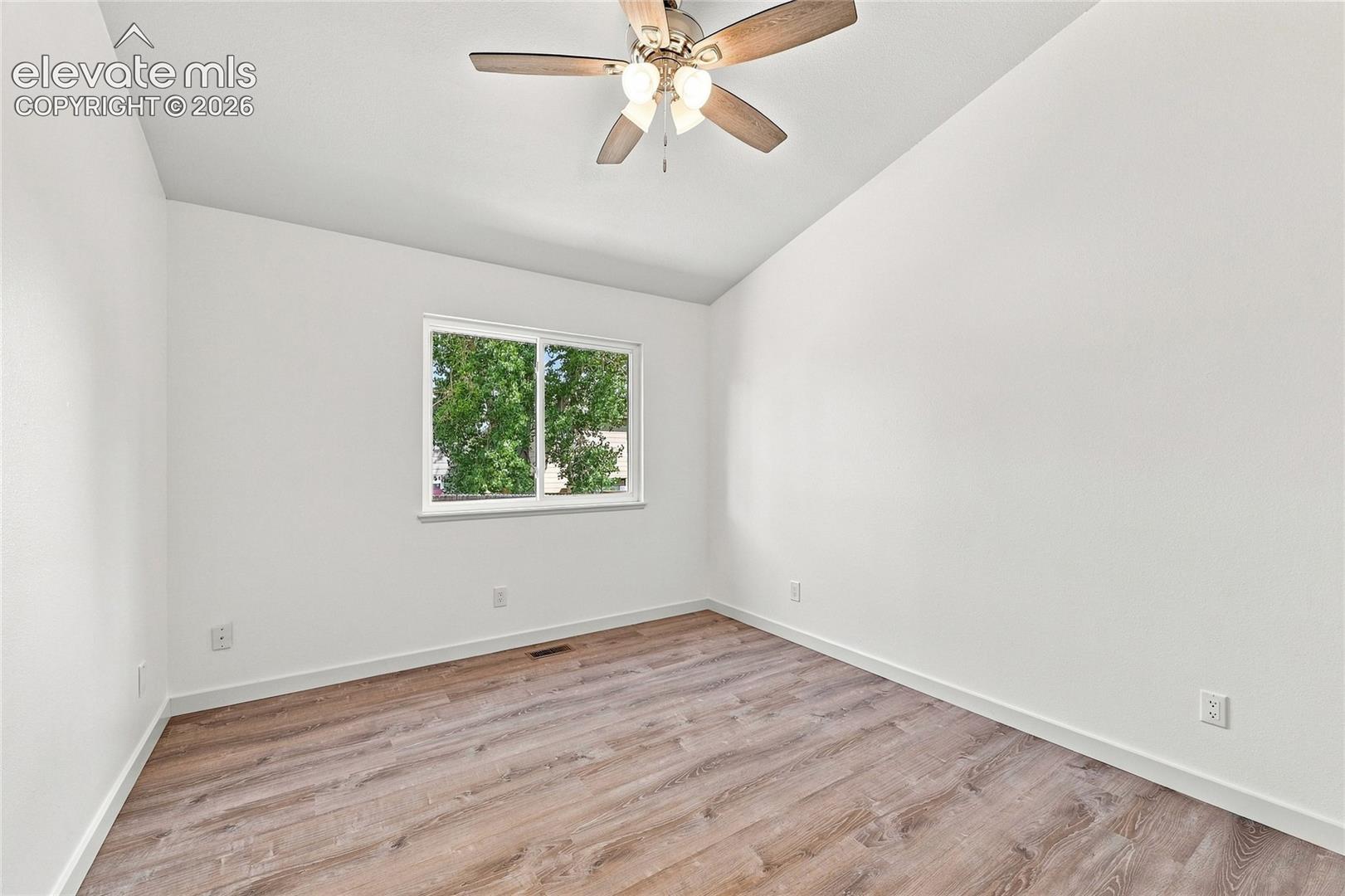 Vaulted ceiling with a ceiling fan, wood-finish flooring, and a window providing natural illumination