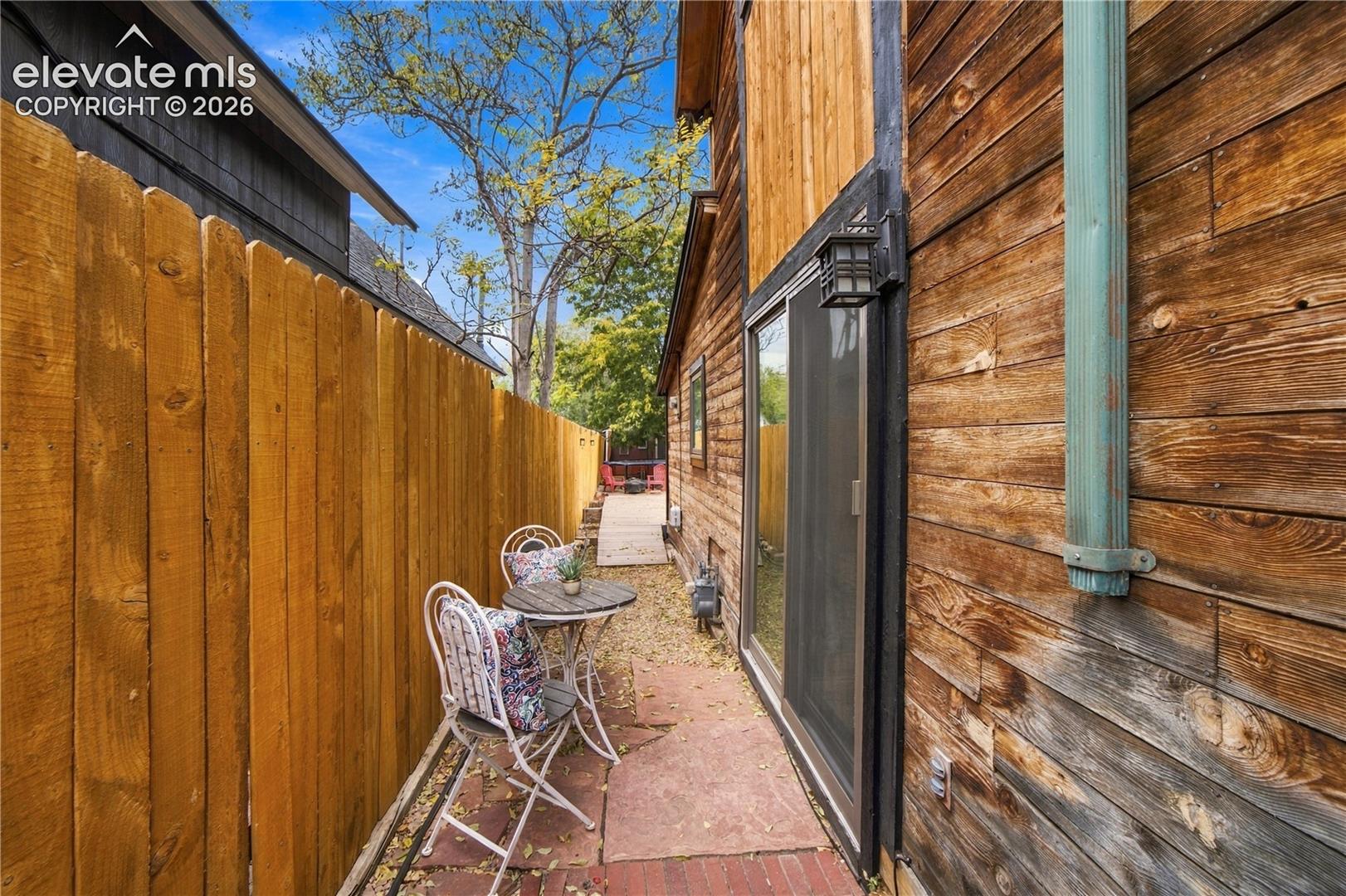 Exterior side yard featuring horizontal wood siding, a full-height wood privacy fence, stone paver pathway, and wall-mounted exterior lighting