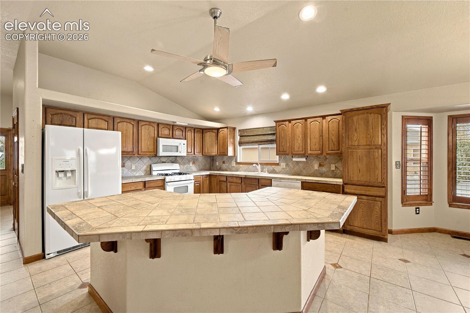 Kitchen featuring a tile-surfaced peninsula, natural wood cabinetry, recessed lighting, vaulted ceilings, and a bay window
