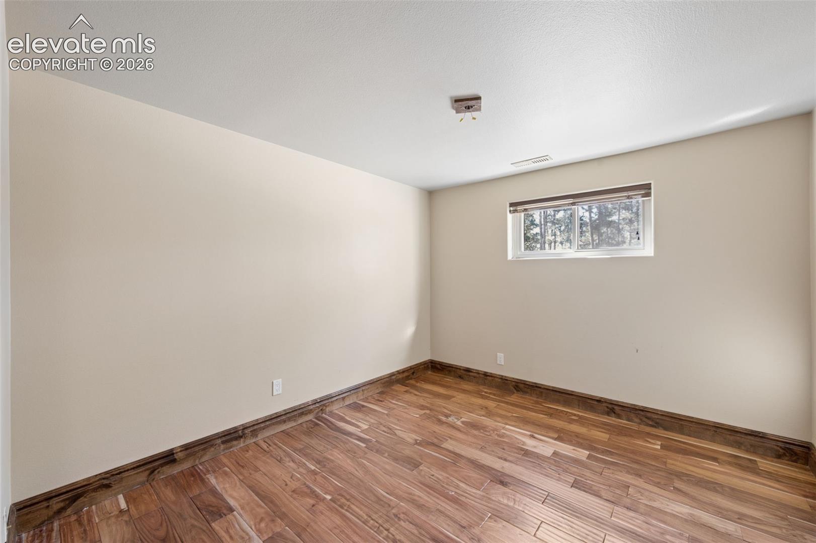 Neutral interior space featuring wood-finish flooring and a single horizontal window