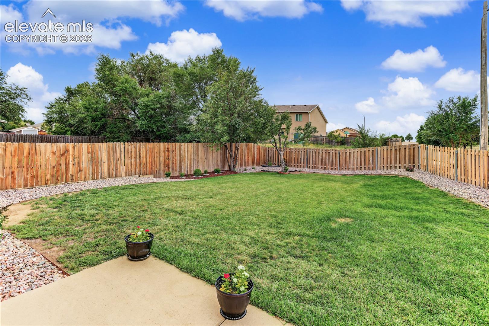 Expansive backyard featuring a large grass area, wood privacy fencing, and a concrete patio