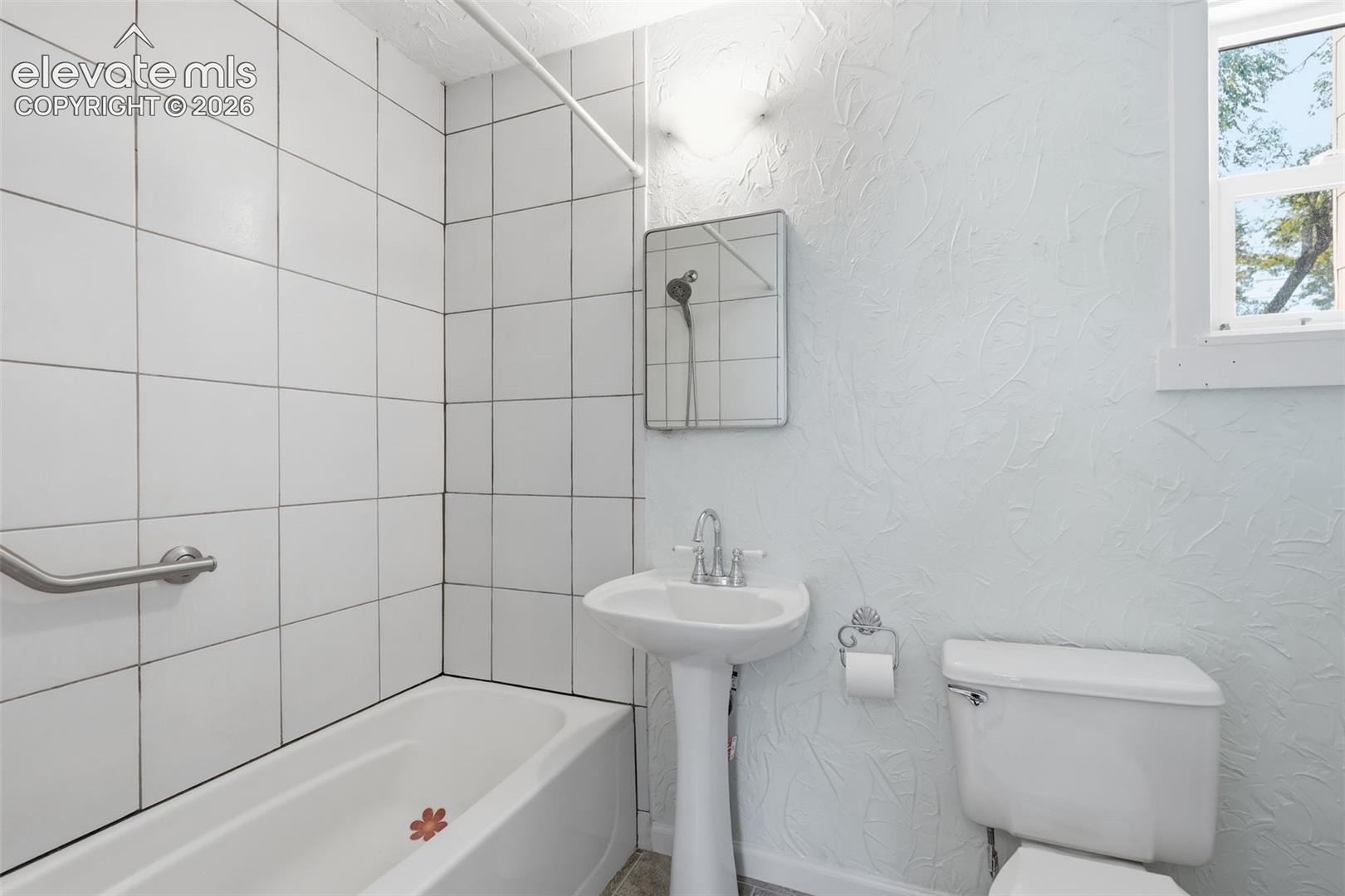 Main-floor bathroom featuring a pedestal sink, white toilet, and tub with white tile surround.