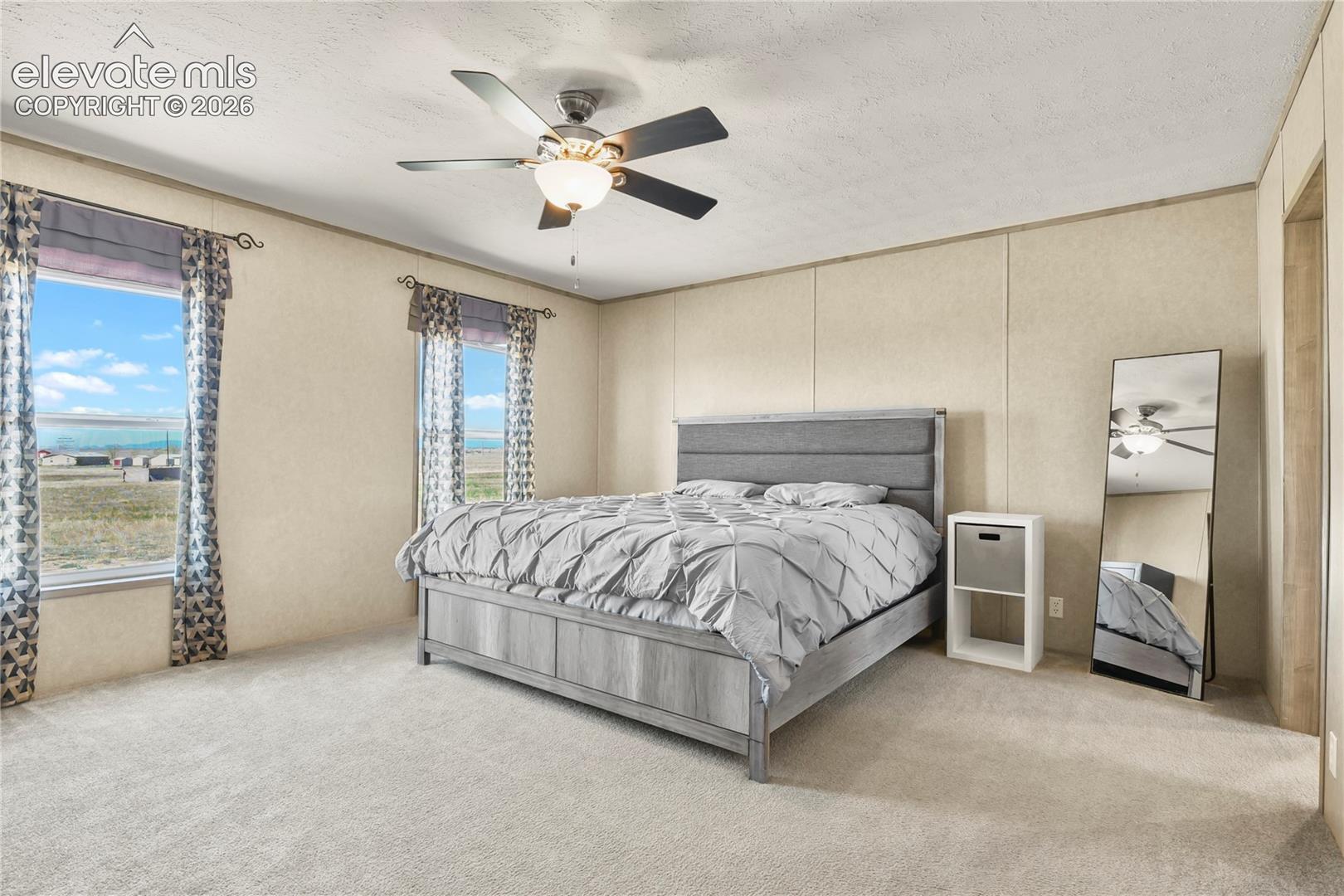 Bedroom featuring neutral wall paneling, carpeting, dual windows, and a ceiling fan with integrated lighting