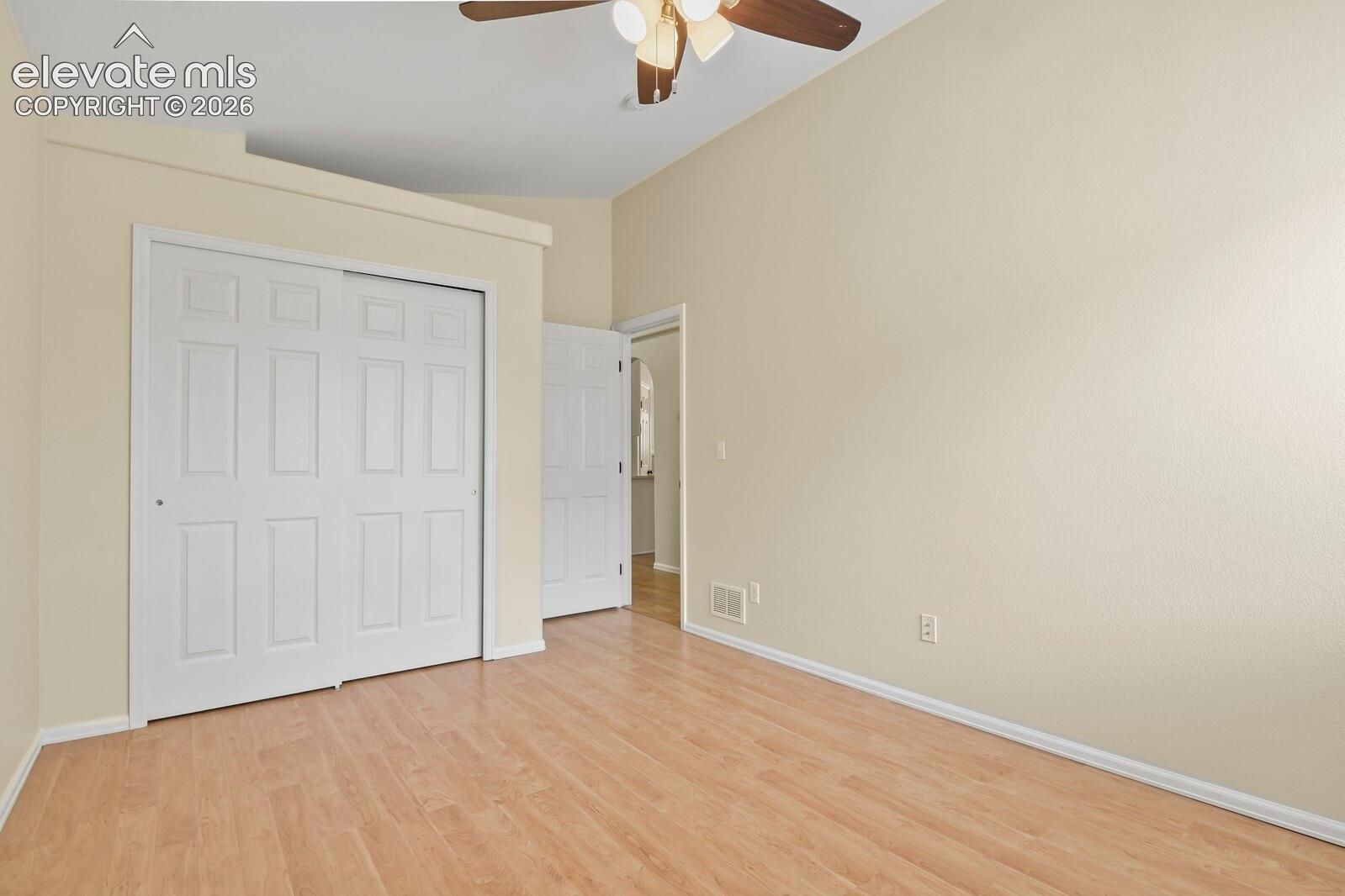 Spacious room featuring vaulted ceilings, wood-finish flooring, a ceiling fan with integrated lighting, and white bi-fold closet doors