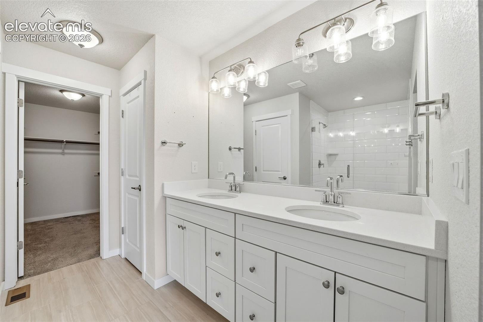 Double vanity with white cabinetry, light-toned countertops, and brushed nickel hardware
