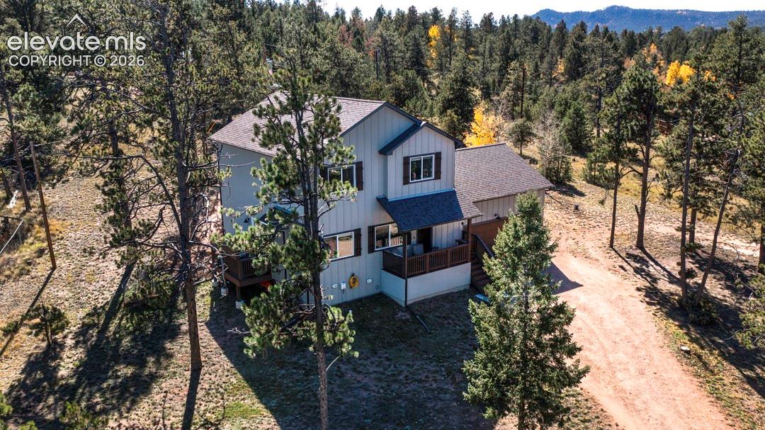 Two-story residence with vertical board-and-batten siding, pitched shingle roof, wood-railed deck, and a natural setting featuring mature pine trees and mountain topography