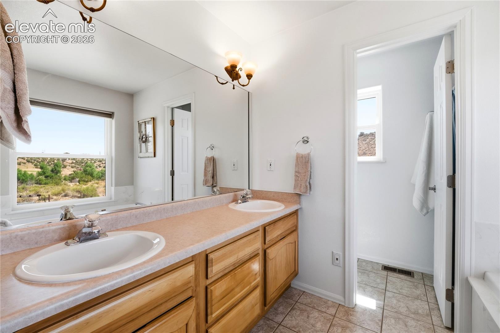 Bathroom featuring a dual vanity with light wood cabinetry, a large wall-mounted mirror, and a window with natural scenery