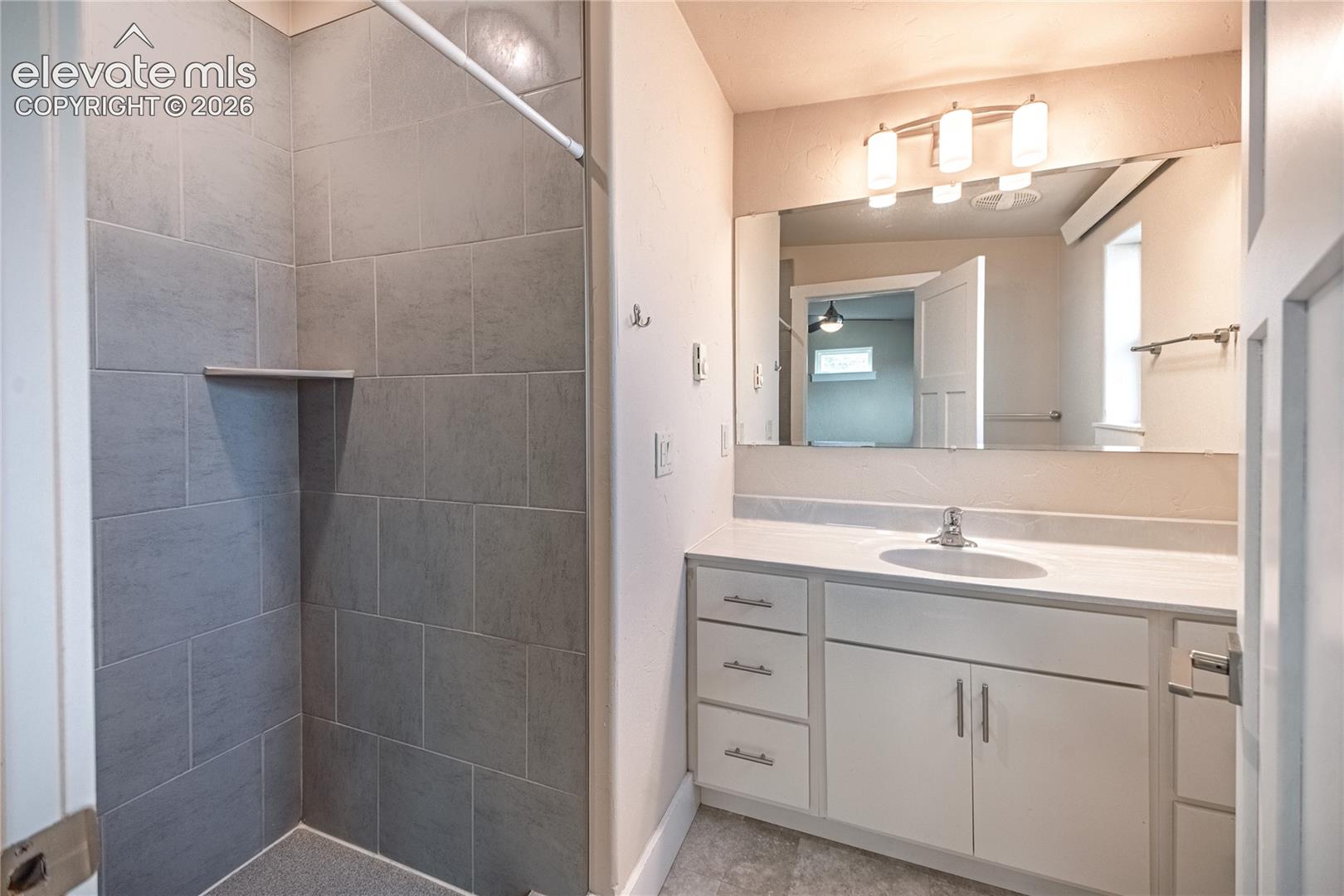 Bathroom vanity featuring a single sink, white cabinetry with silver-tone hardware, and a large mirror with overhead lighting
