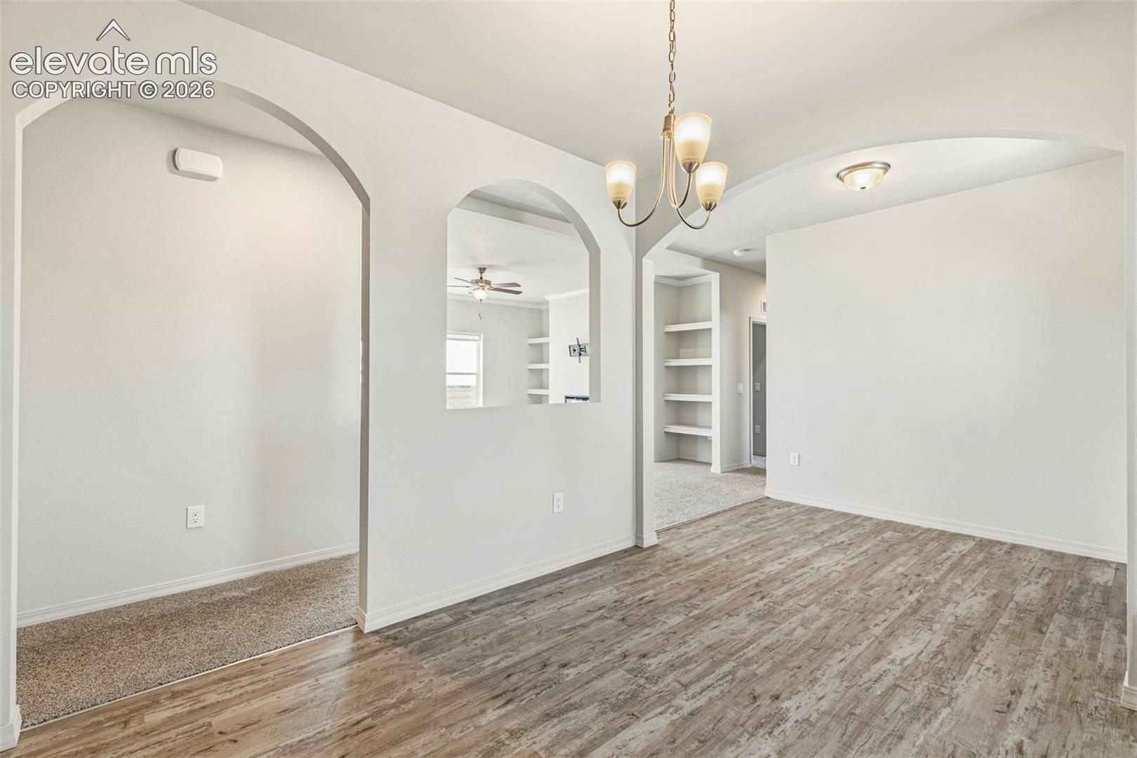 Dining area featuring wood-finish flooring, a contemporary chandelier, and an arched entry