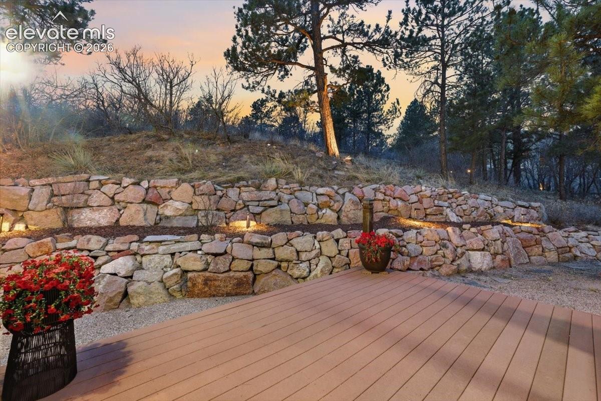 Spacious wood-finish deck with integrated lighting, tiered stone retaining walls, and mature landscaping