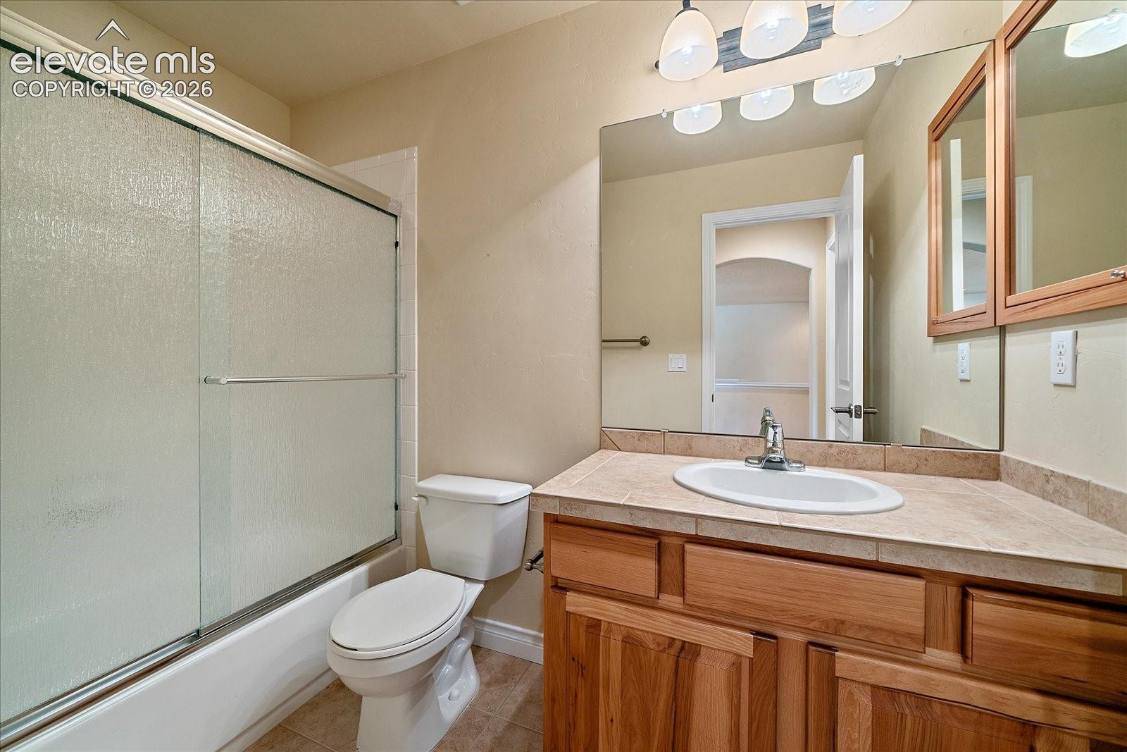 Bathroom featuring a wood vanity with a tile countertop, integrated sink, large wall-mounted mirror, and a sliding glass shower door