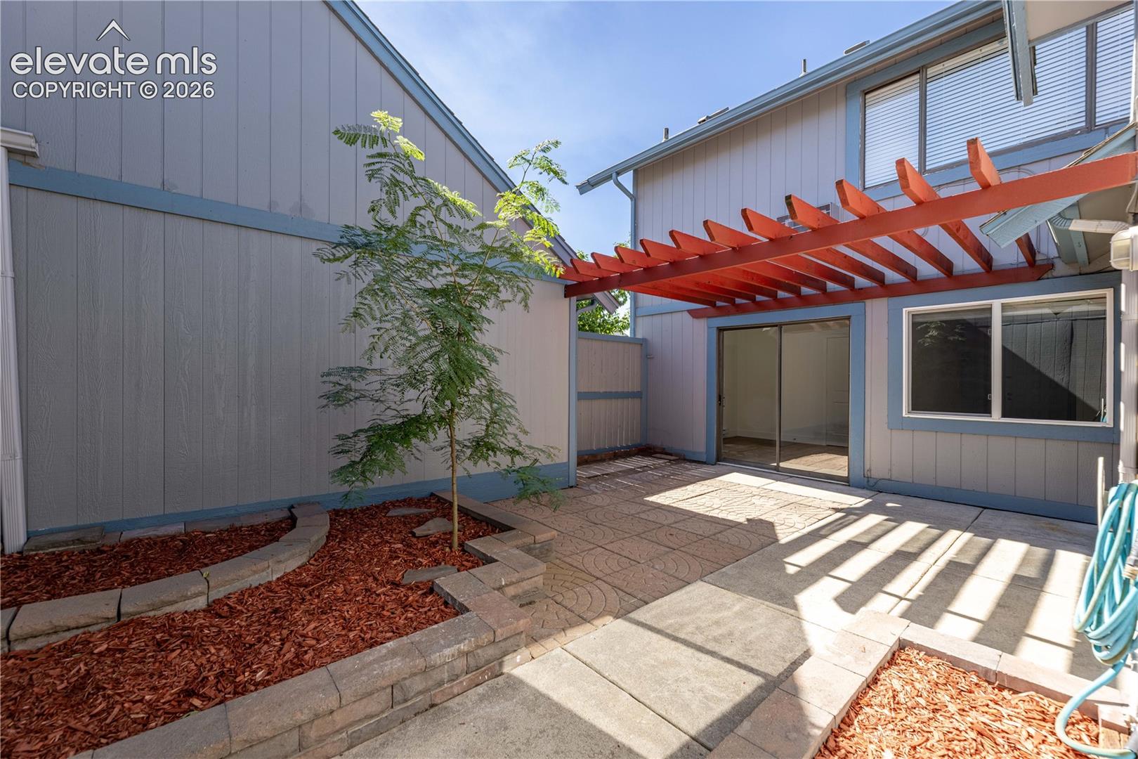 Private patio featuring a stamped concrete surface, integrated wood pergola, terraced planter beds with stone block retaining walls, and vertical wood siding