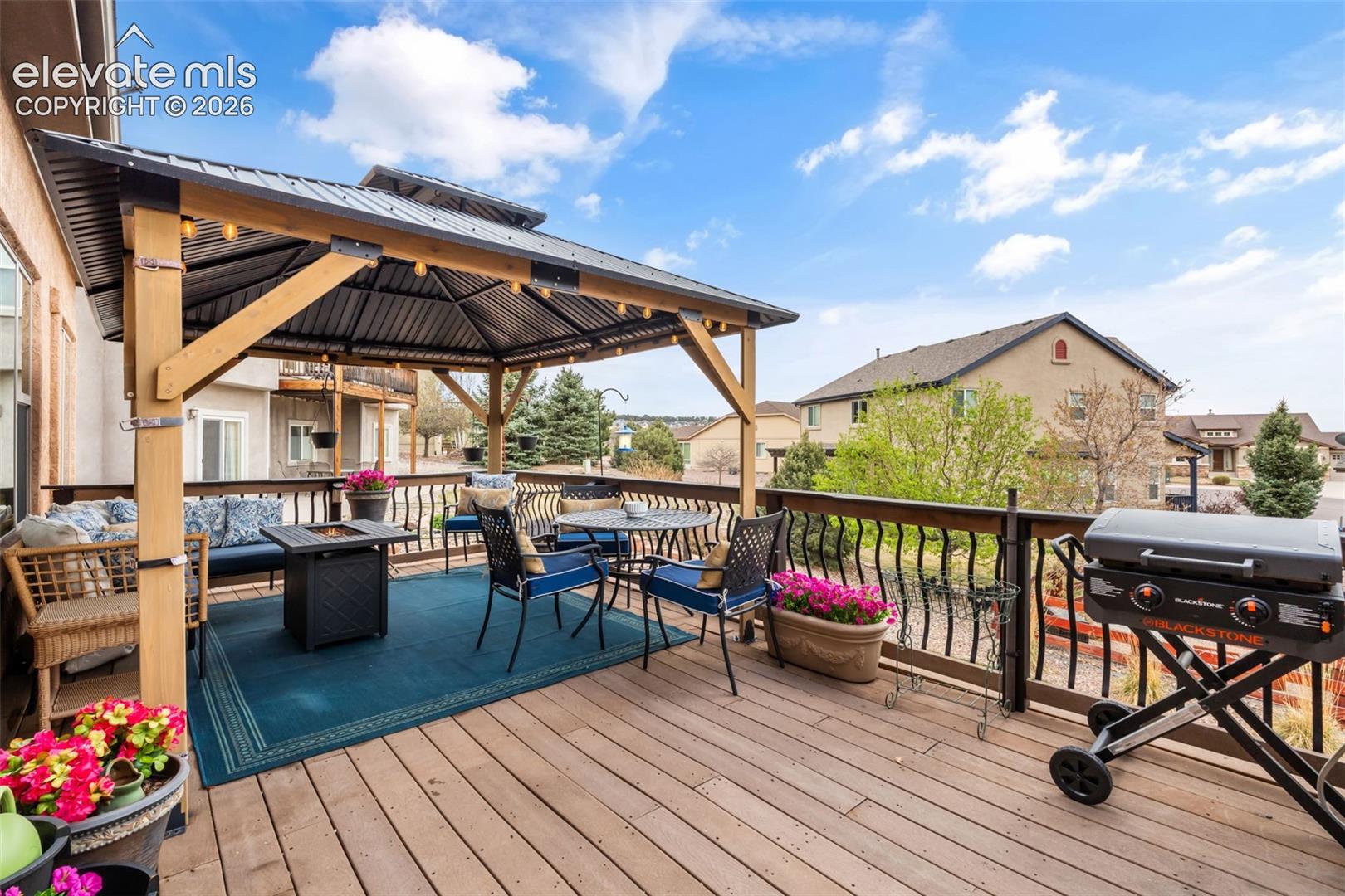 Expansive outdoor deck featuring a built-in pergola with a metal roof and string lighting, wood-finish decking, and wrought iron railings