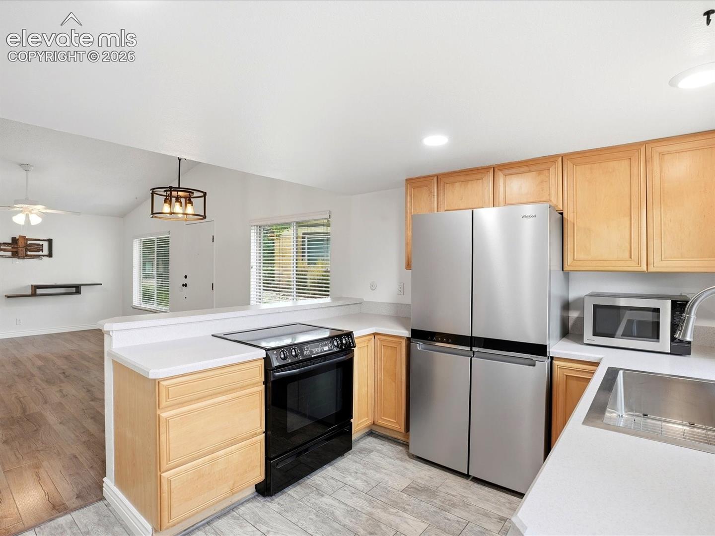 Kitchen featuring light wood cabinetry, white countertops, stainless steel refrigerator, black electric range, and tile flooring