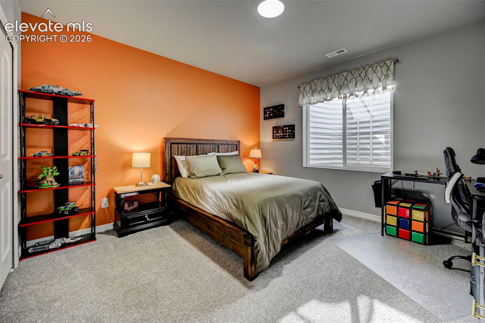 Bedroom featuring light gray carpet flooring and a statement wall in orange