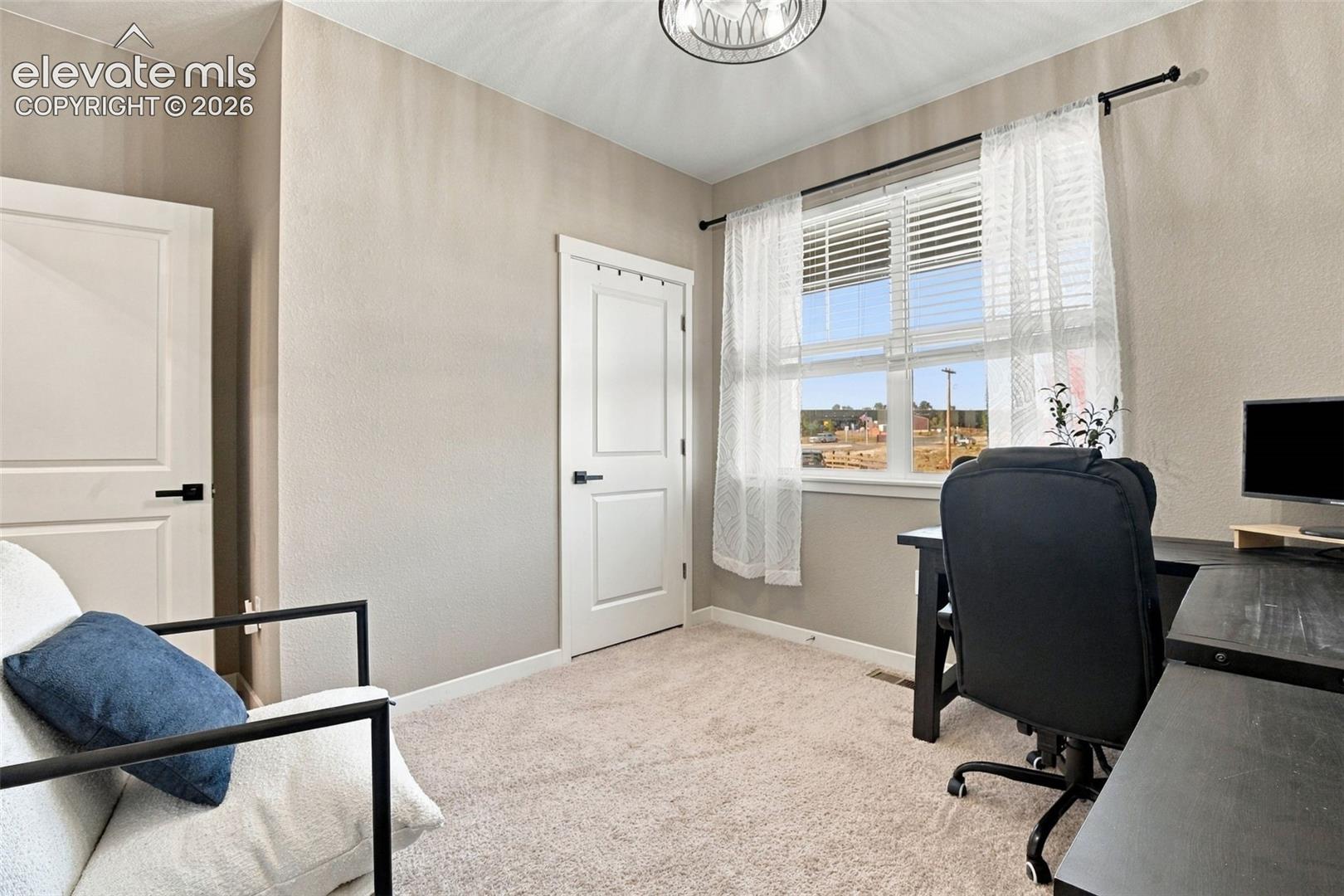 Neutral-toned interior featuring wall-to-wall carpeting, two-panel interior doors with matte black hardware, and a single-hung window with horizontal blinds and drapery hardware