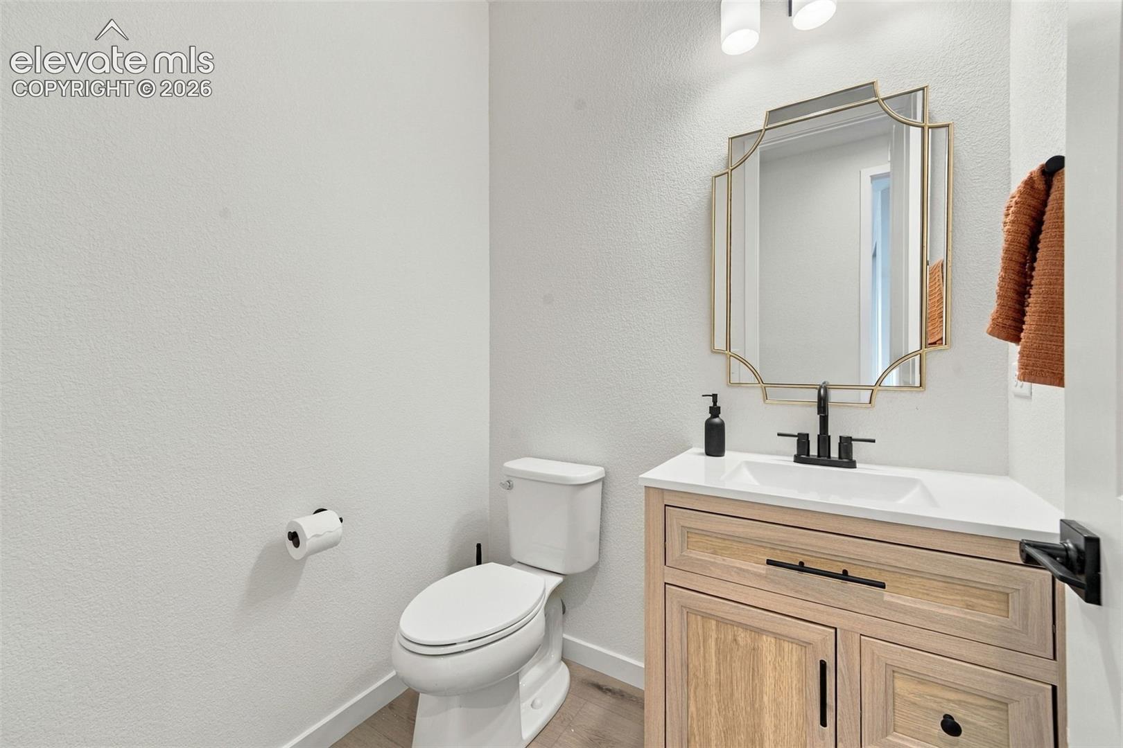 Custom wood-finish vanity with a white countertop and rectangular integrated sink, matte black faucet hardware, and a geometric-framed vanity mirror