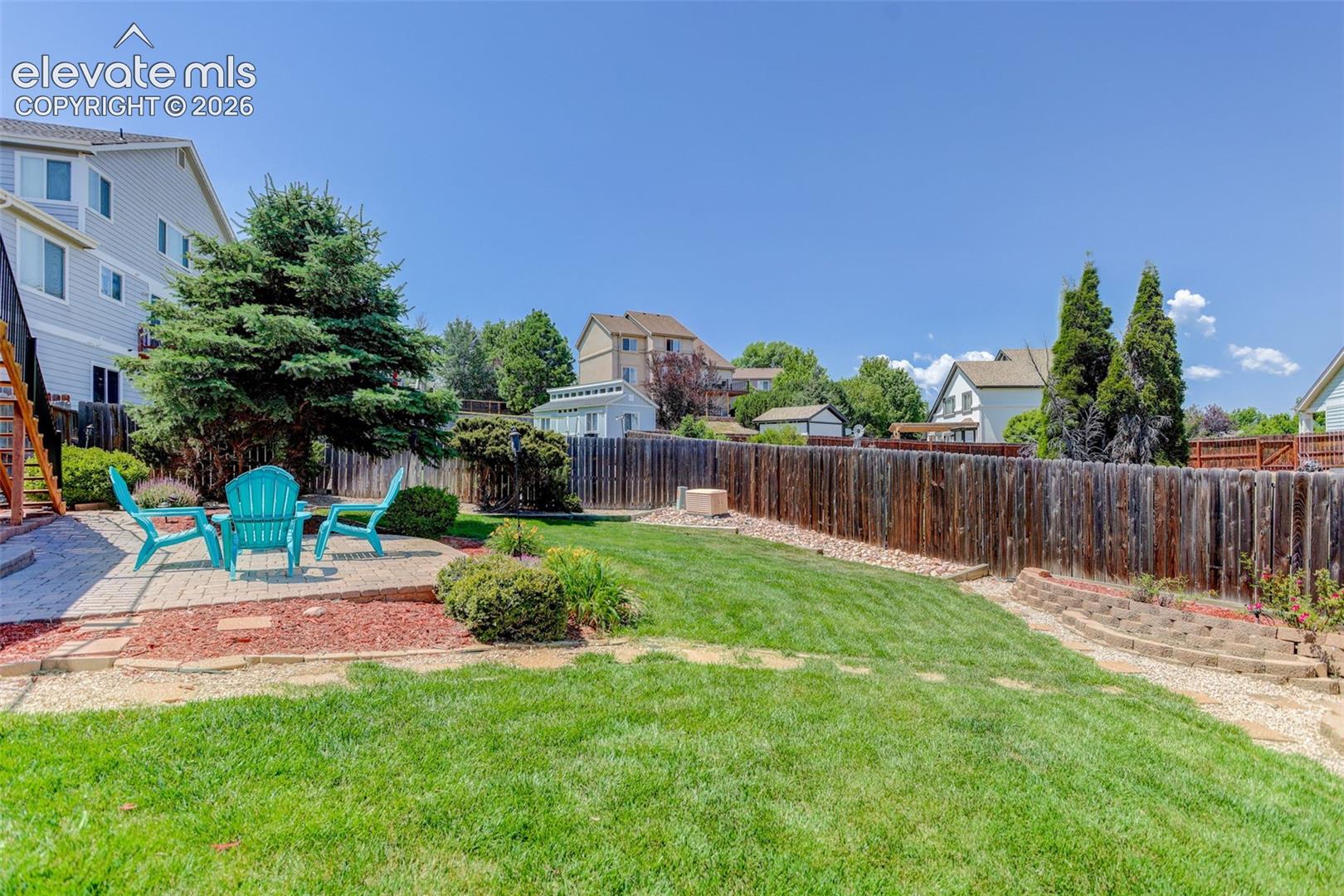 Expansive backyard featuring a paver patio area, a wood privacy fence, a manicured lawn, and mature trees