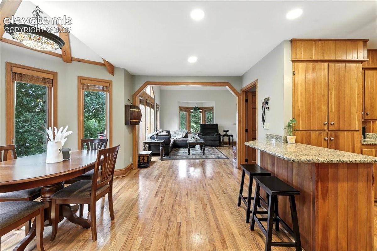 Hardwood flooring, vaulted ceilings with decorative beams, arched doorways, kitchen peninsula with stone-finish countertops, and natural wood cabinetry