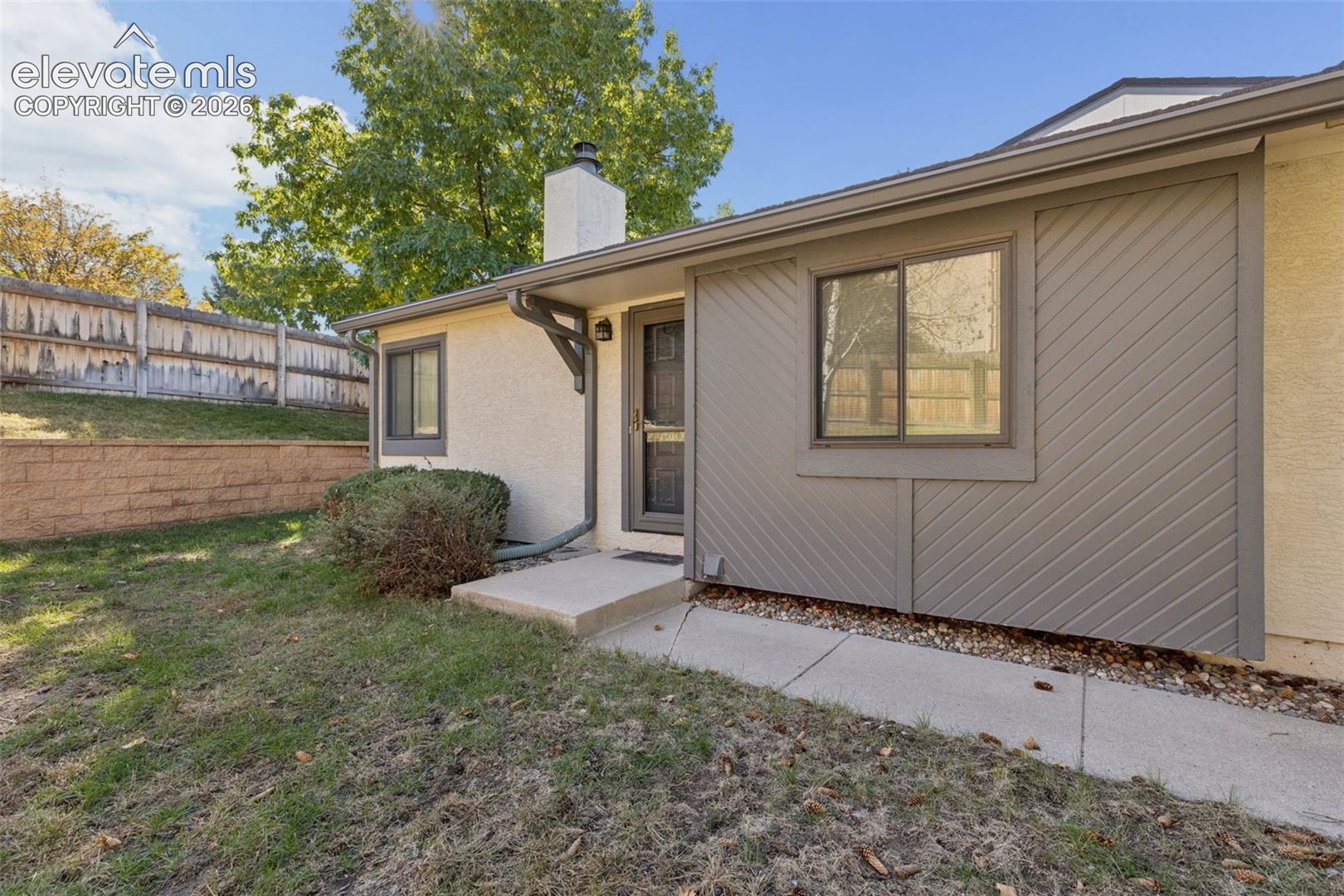 Exterior featuring stucco and diagonal wood siding, concrete walkway, masonry chimney, and stone retaining wall