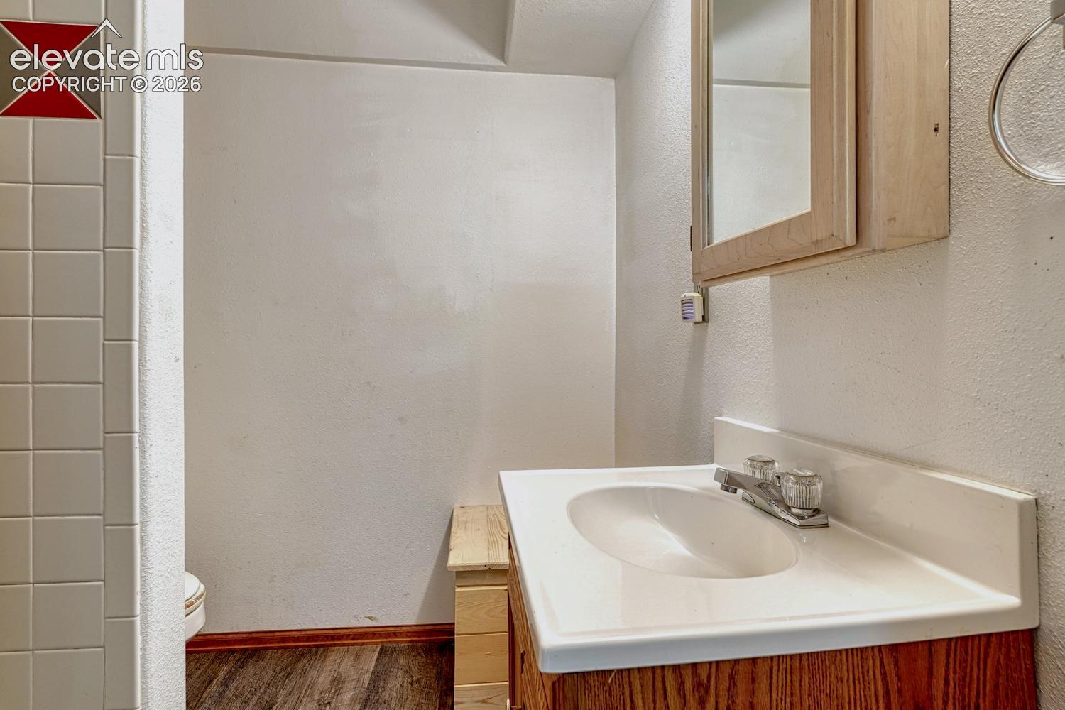 White ceramic tile wall with red accent, wood-finish flooring, vanity with integrated white sink, wood-finish cabinet with medicine mirror