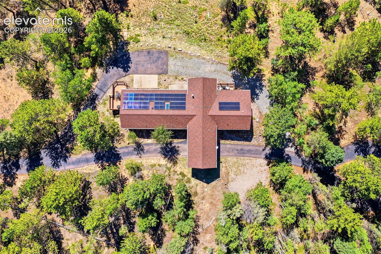Expansive property featuring a cross-shaped roofline, multiple solar panel arrays, and a winding paved driveway